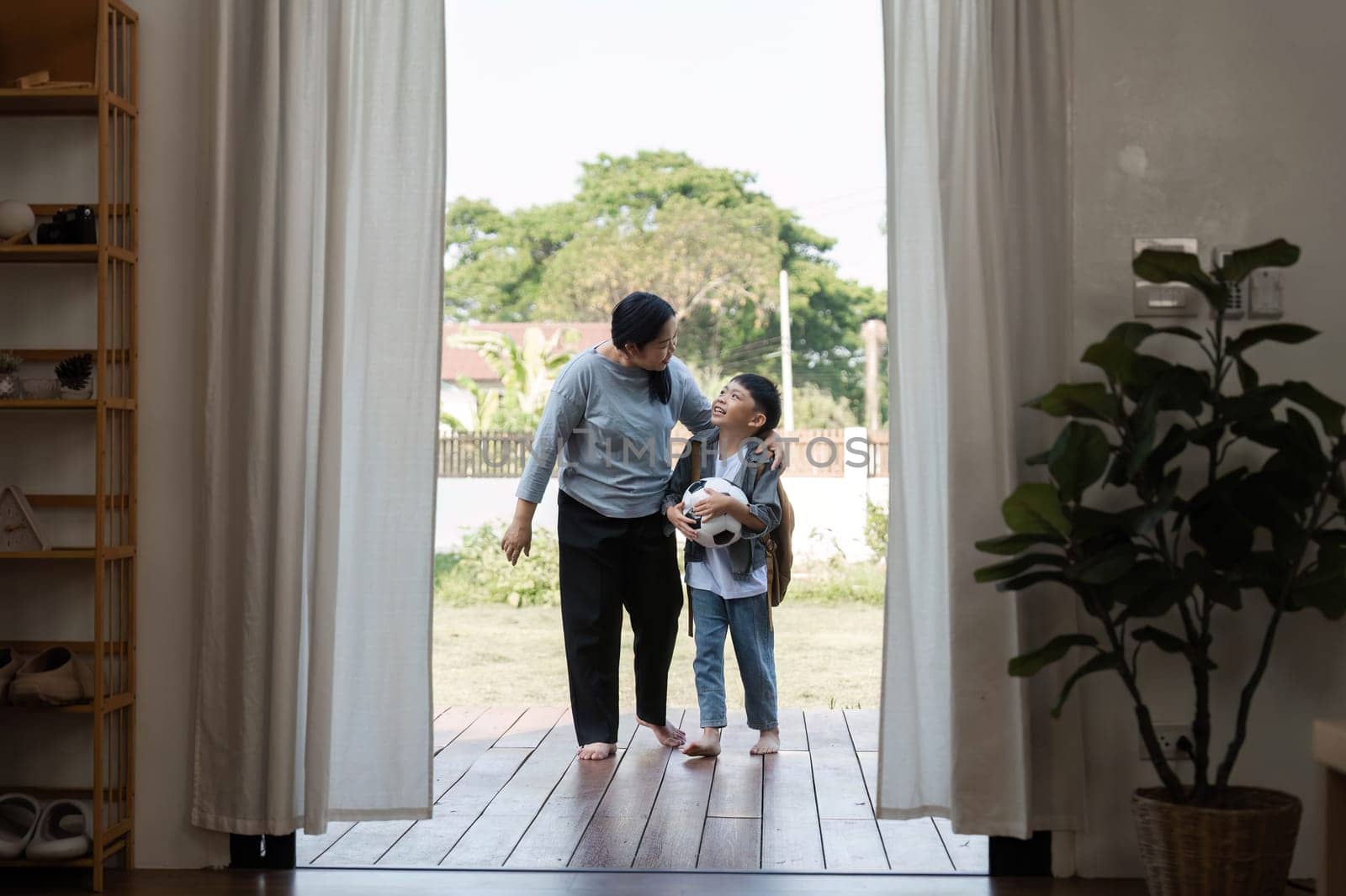 A mother and her son share a tender moment as they step onto the porch, ready for an outdoor adventure, highlighting their close bond.