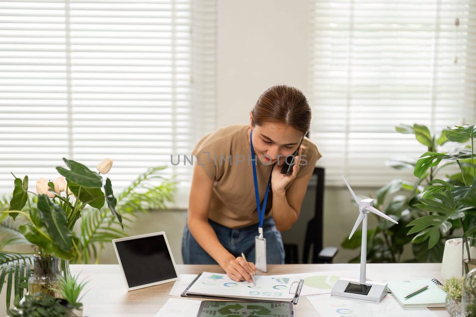 A dedicated young woman organizing sustainability documents while on a phone call, highlighting her commitment to eco-conscious initiatives.