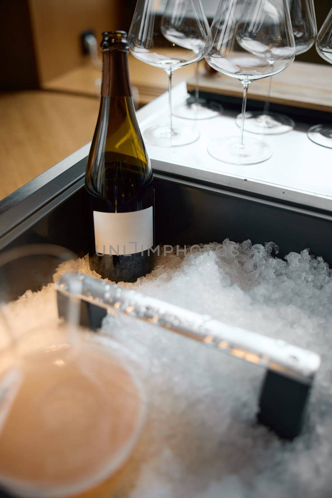 Bottle of champagne is cooled in a niche with ice in the restaurant, local lighting, wine cabinet, decanters for sparkling wine. High quality photo