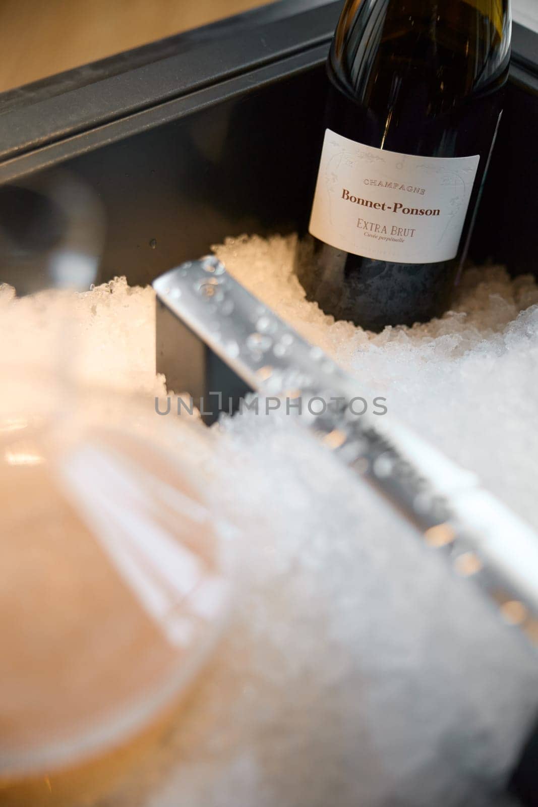 Russia, St.Petersburg, 29 April 2025: Bottle of champagne brand Bonnet-Ponson is cooled in a niche with ice in the restaurant, local lighting, wine cabinet, decanters for sparkling wine. High quality photo