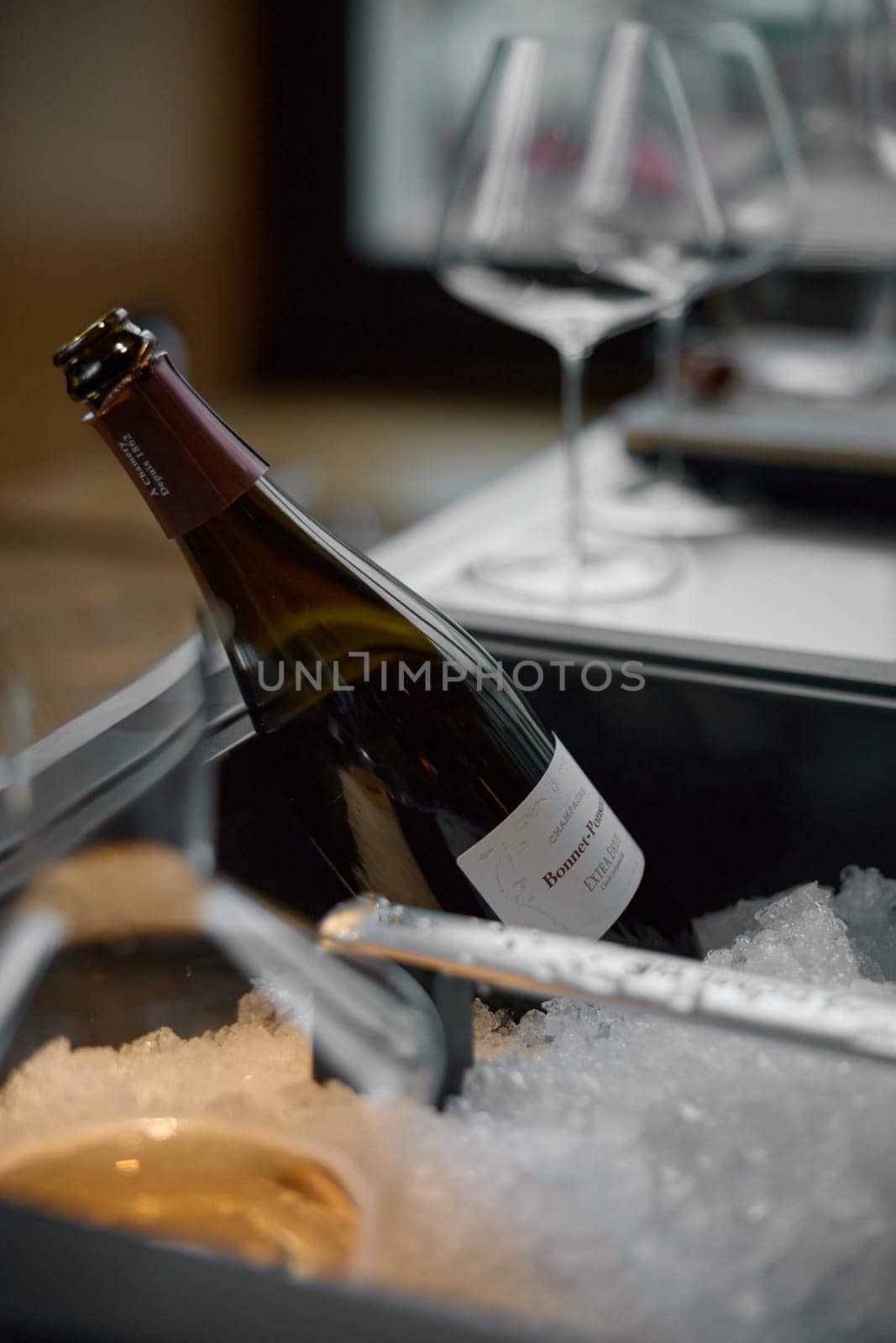 Russia, St.Petersburg, 29 April 2025: Bottle of champagne brand Bonnet-Ponson is cooled in a niche with ice in the restaurant, local lighting, wine cabinet, decanters for sparkling wine. High quality photo