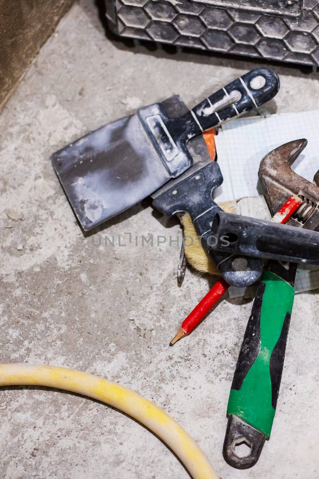 On the floor, there is a spatula, a wrench, a pencil, and a hose scattered about, creating a cluttered scene of various tools and items