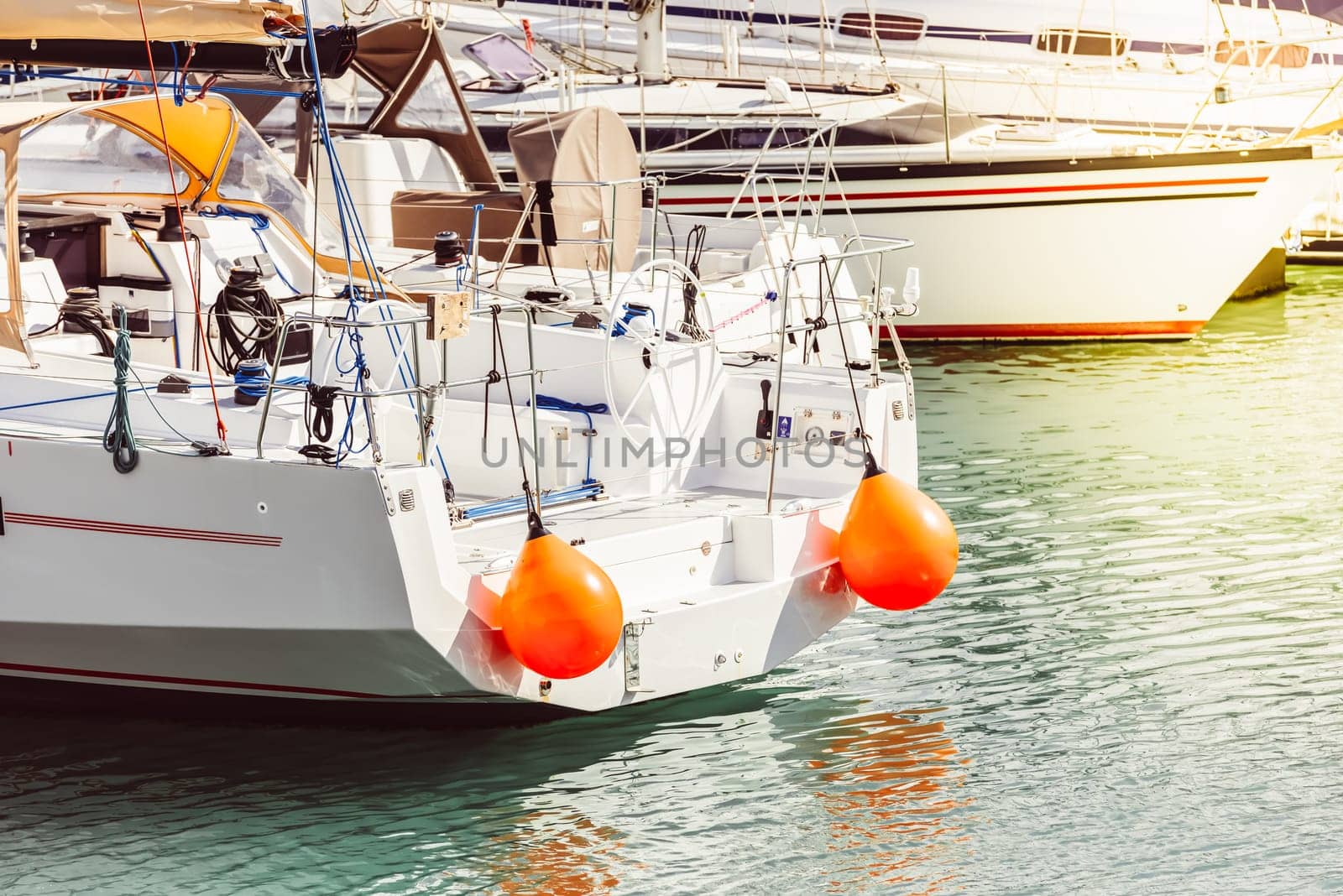 Yacht with orange buoys docked at marina, calm sea reflecting light, 