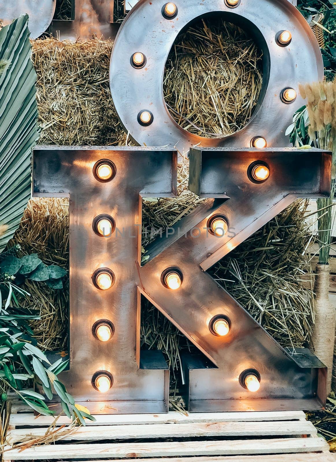 Illuminated metal letter K against a rustic hay background, 
