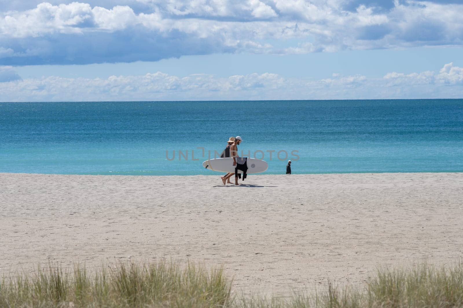Tauranga New Zealand - March 22 2023: Mount Maunganui Main Beach background scene with people walking carrying surfboard.