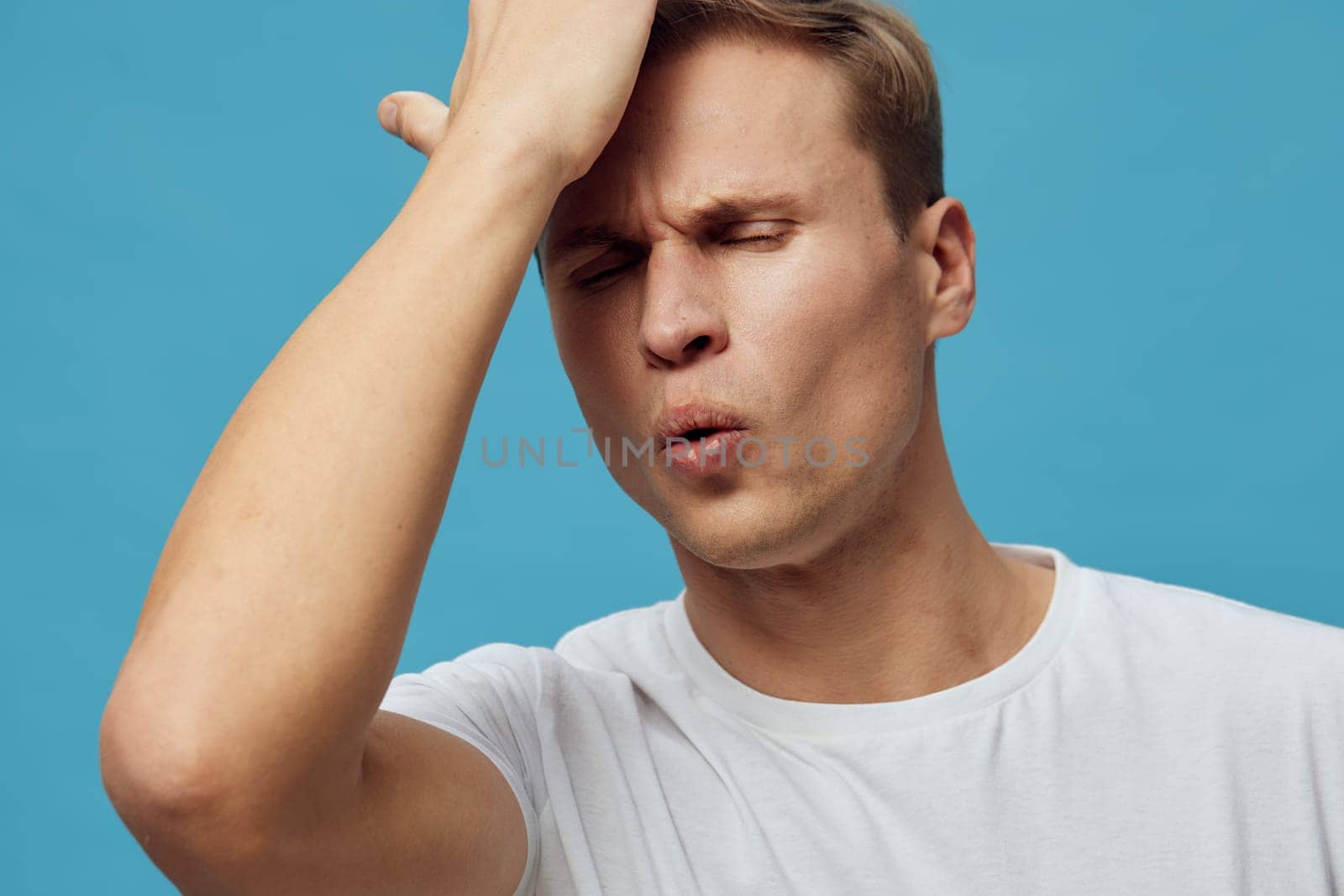 frustrated young caucasian man wear white t-shirt with closed eyes touch forehead showing stress and anxiety isolated on grey background mental health and gadgets concept