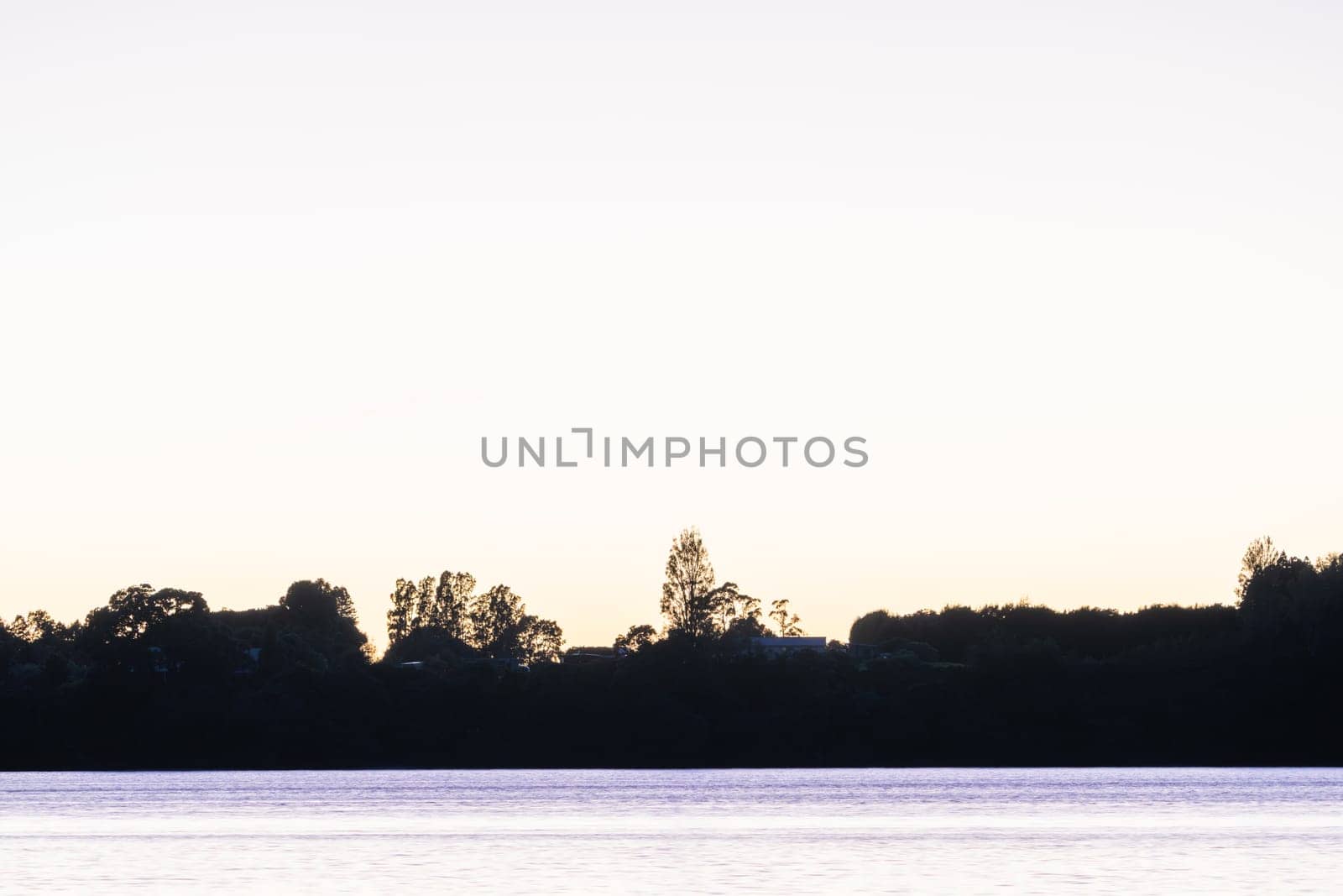 Land and trees in silhouette on horizon at sunrise across bay.