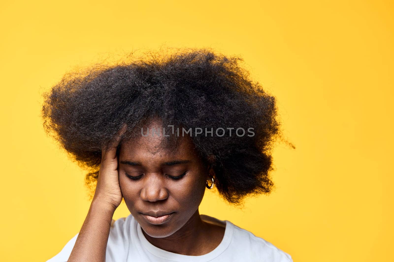 An African woman with voluminous curly hair shows signs of stress and worry The bright yellow backdrop enhances the emotional tone, emphasizing her feelings