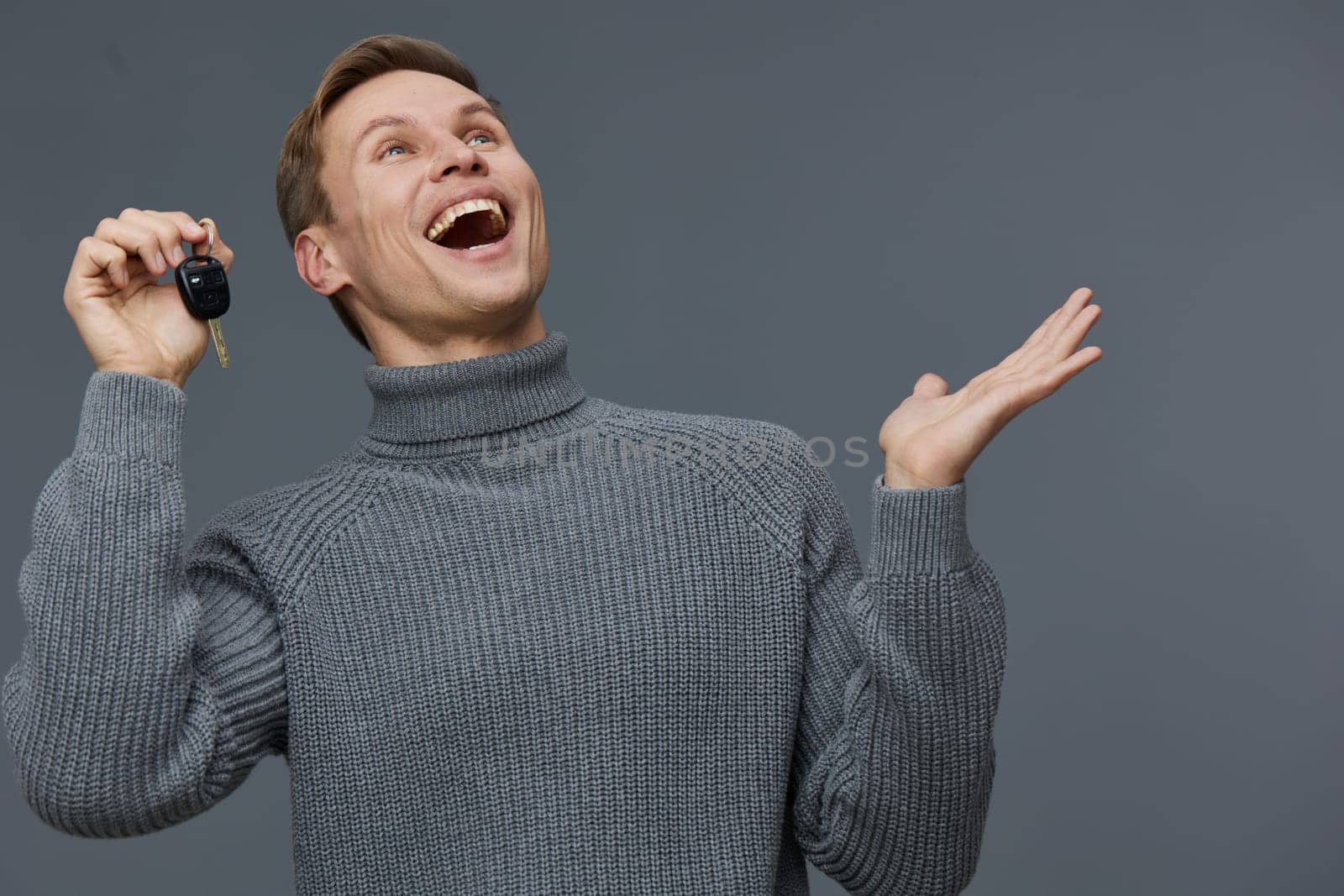 excited man holding car keys in hand wearing knitted gray sweater smile looking up isolated on solid gray background digital nomad freelance technology concept freedom and success