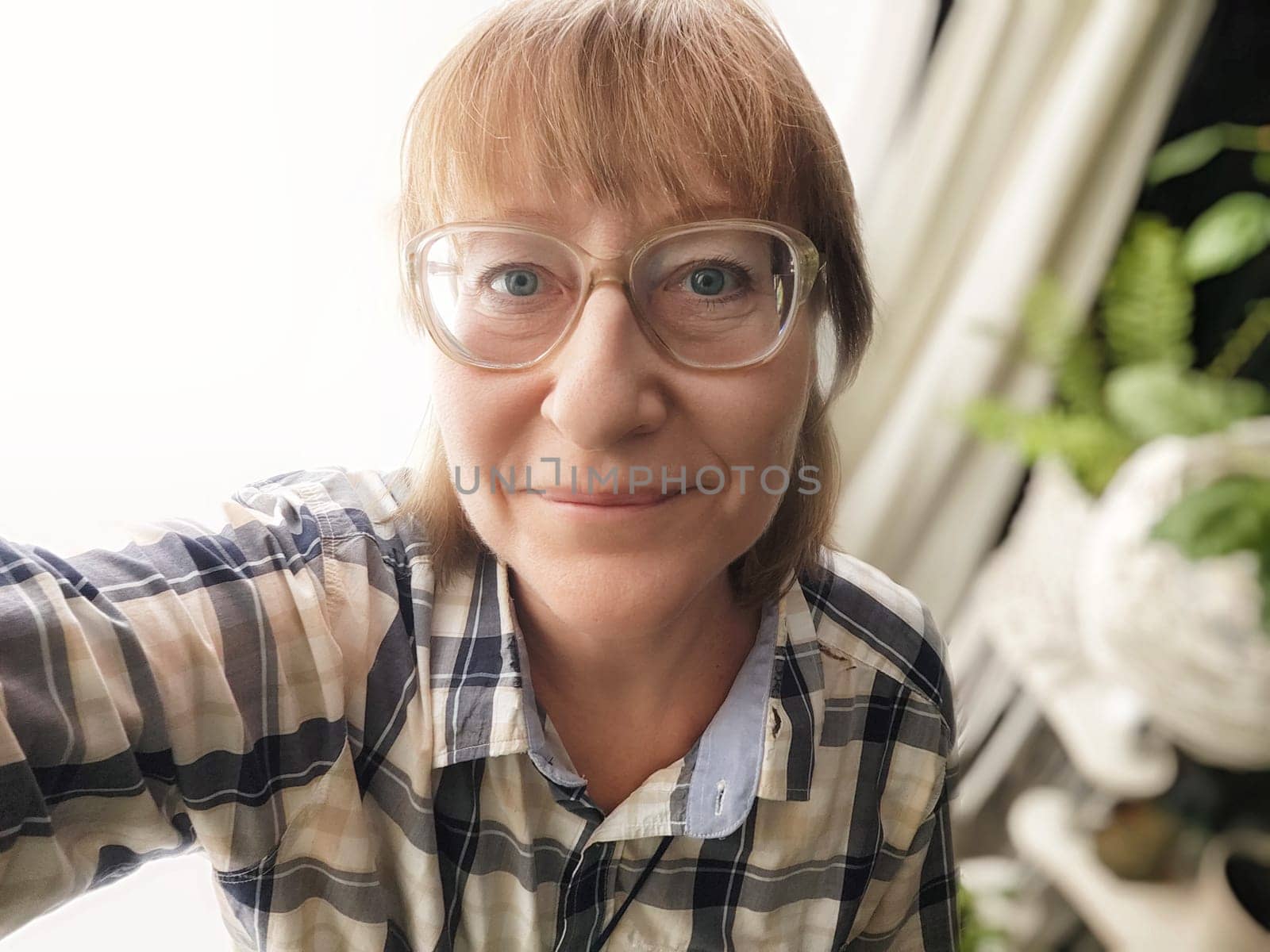 Middle aged woman with glasses enjoys a moment while taking a selfie in her stylish indoor space, showcasing her lifestyle.