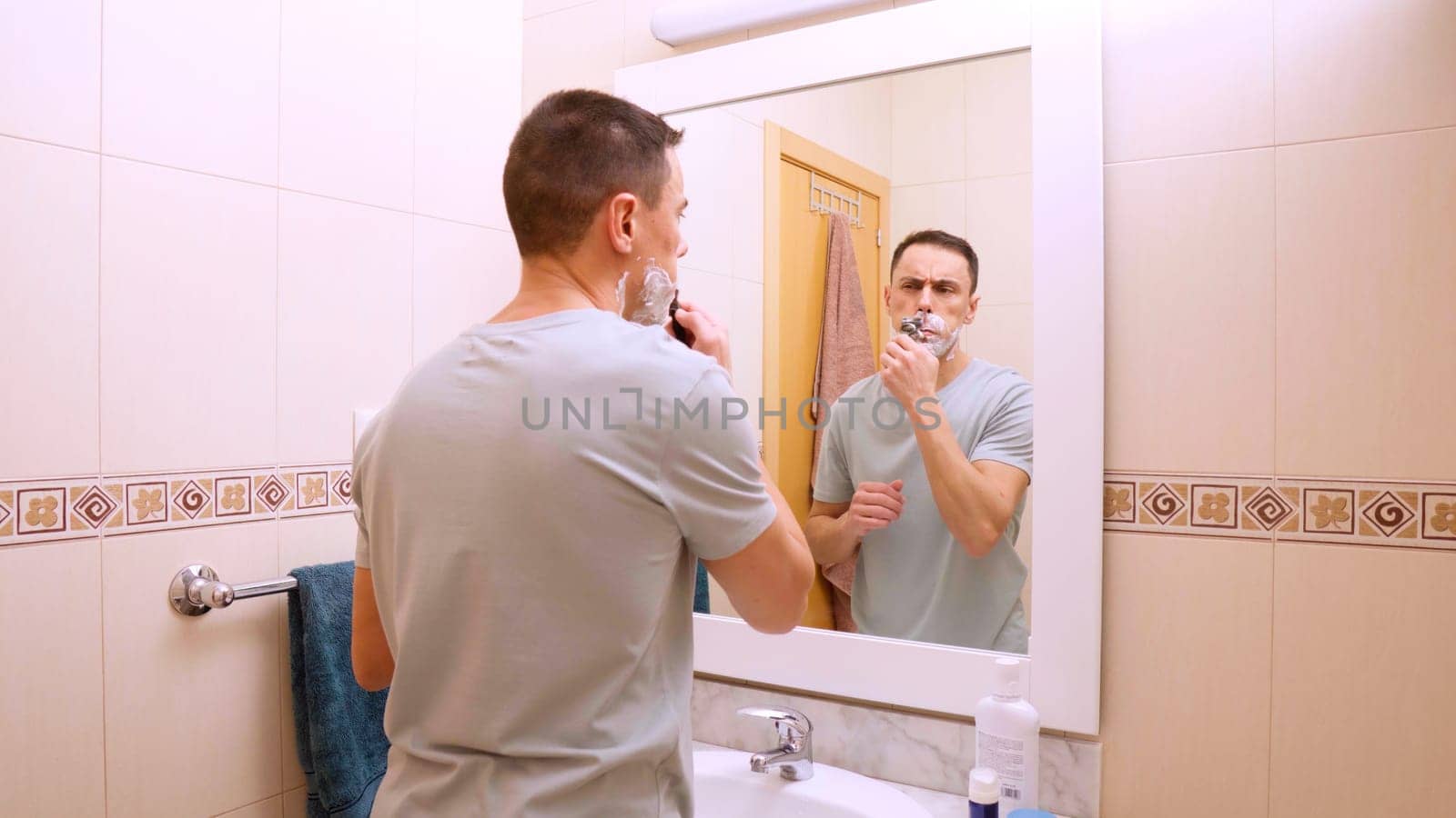 Caucasian man shaving his mustache with shaving cream in front of bathroom mirror