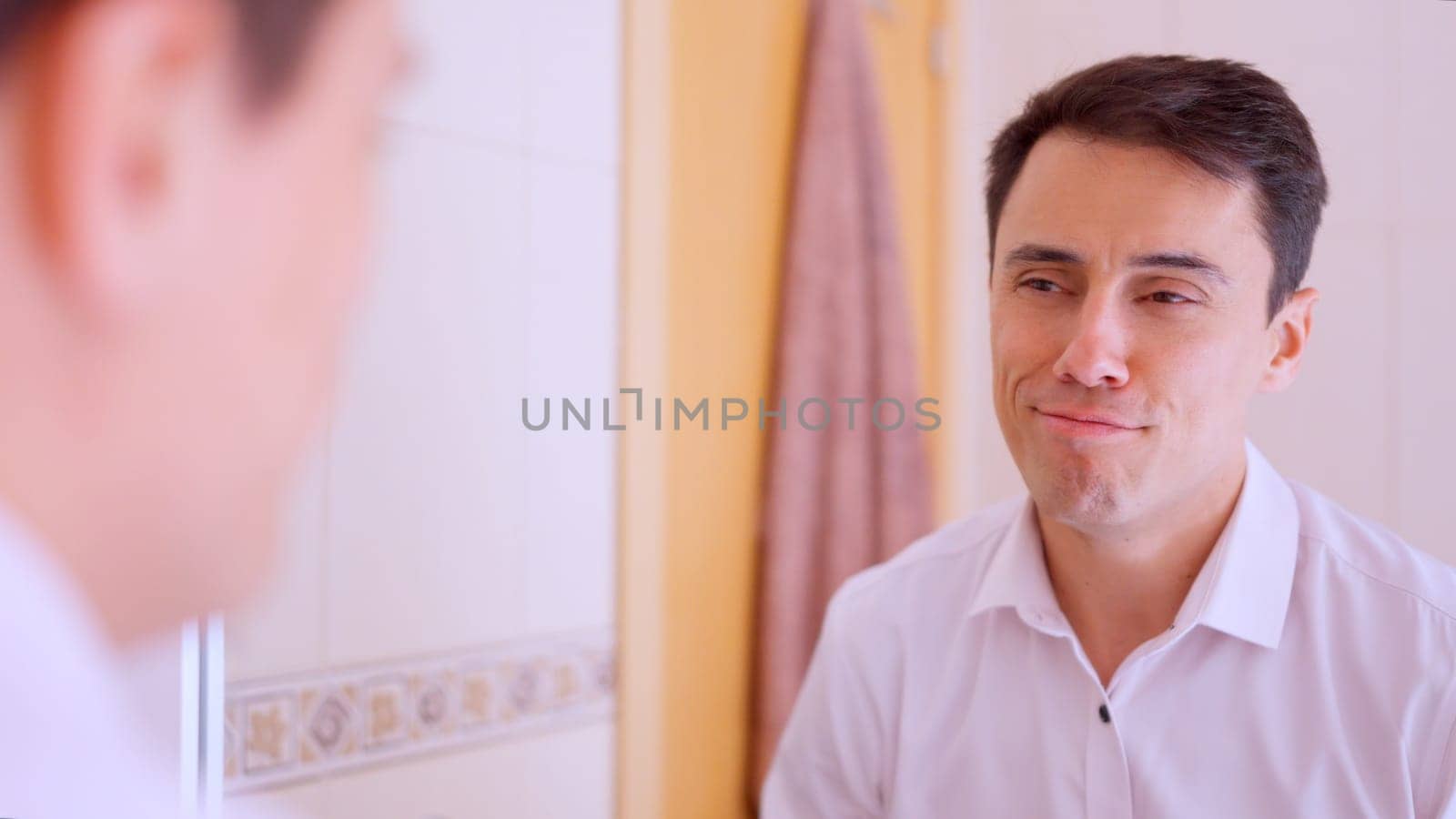 Happy businessman wearing a white shirt looking and smiling at his reflection in a bathroom mirror