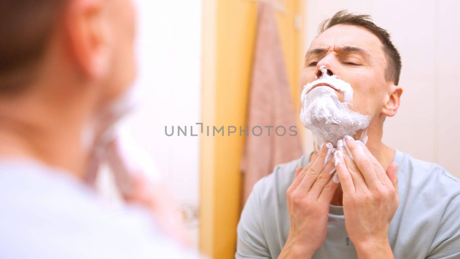 Man applying shaving cream getting ready to shave his beard in bathroom mirror