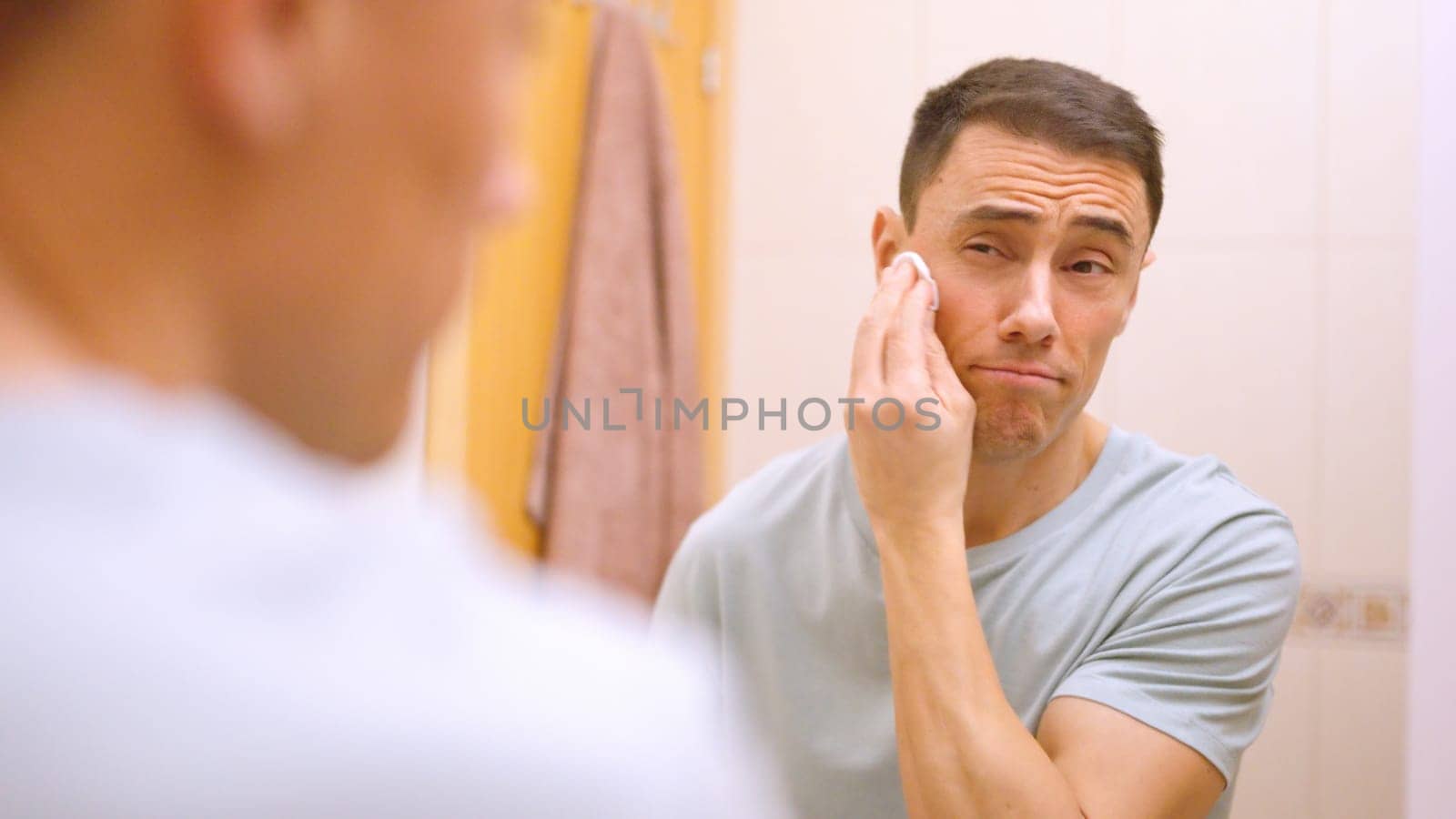 Caucasian man using cotton pad for cleaning face skin after shaving in bathroom