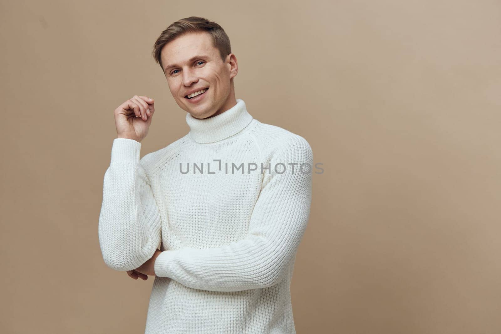 smiling man wearing white turtleneck sweater looking at camera with joyful expression arms crossed isolated on plain beige background studio portrait representing digital detox and mental health concept
