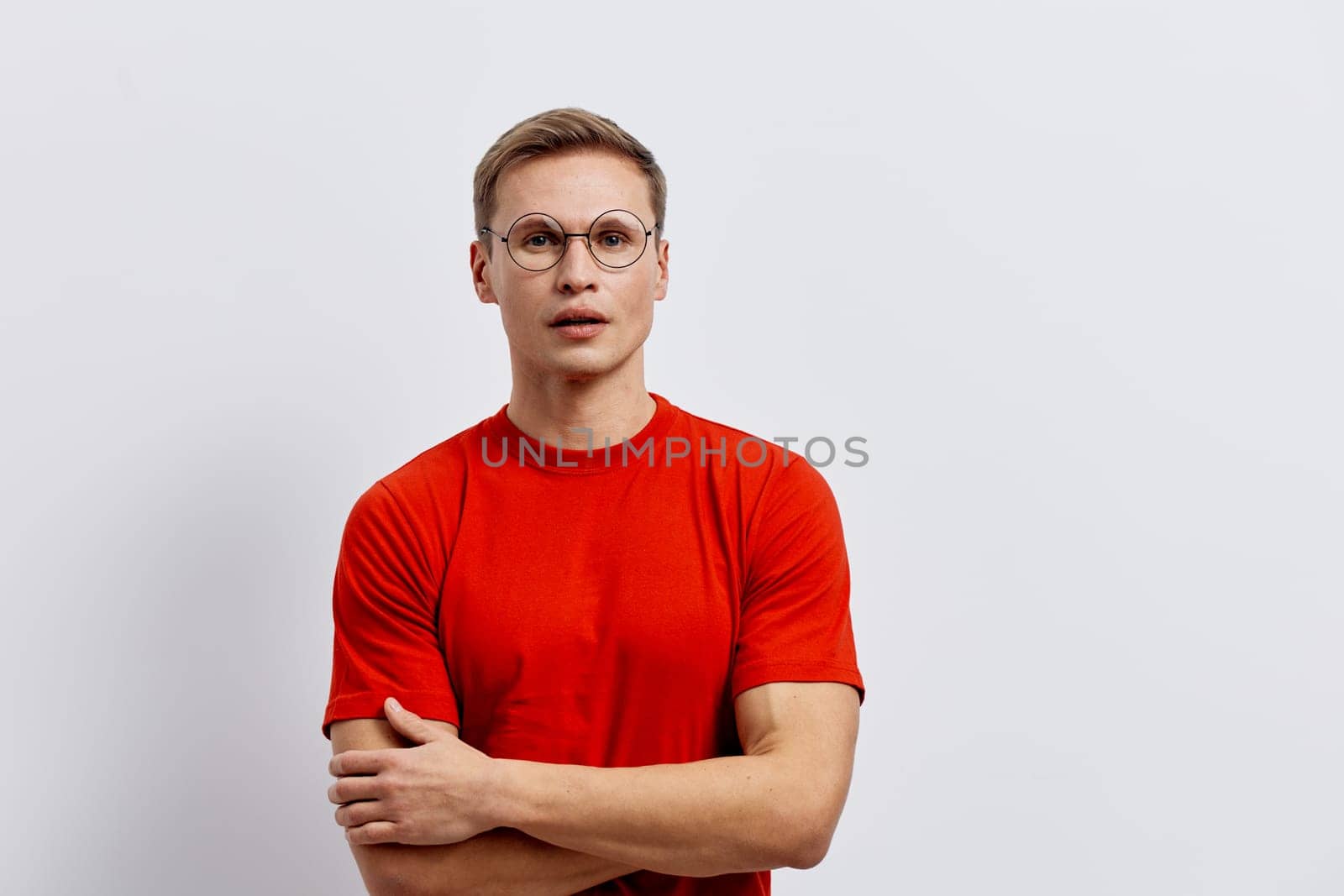 Portrait of a young man wearing a red t-shirt and glasses, standing against a plain white background, looking serious and focused. Studio shot emphasizing confidence and clarity. Concept: self-assurance and professionalism.
