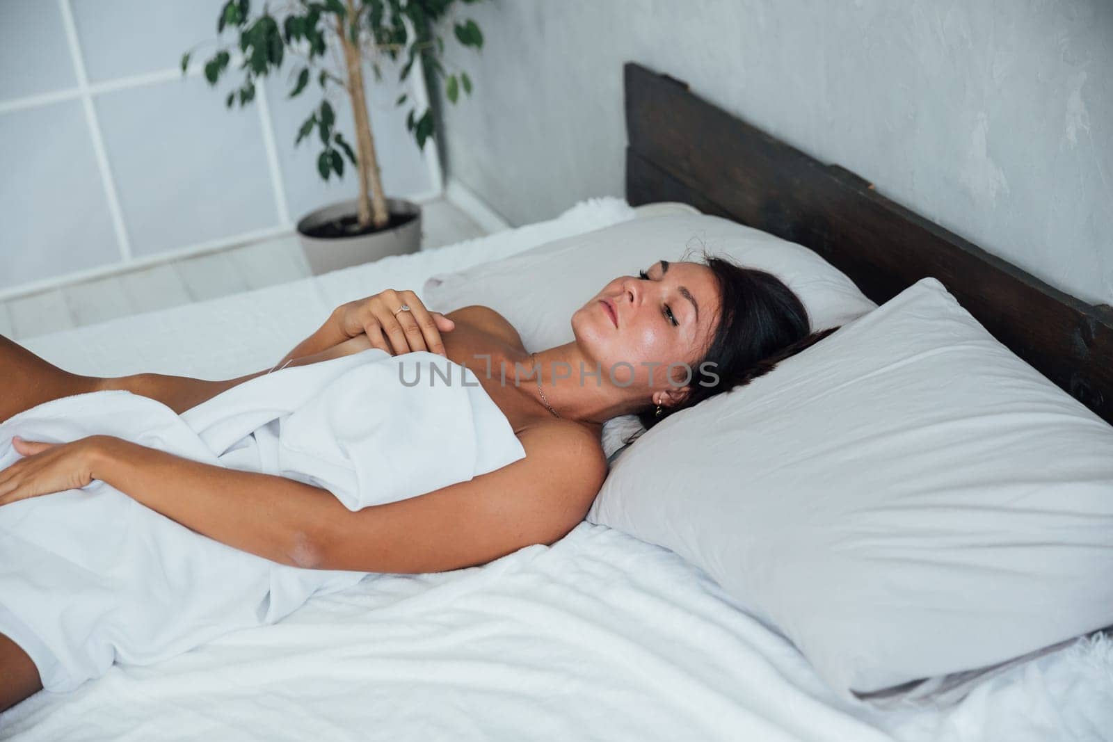 Brunette woman in light lingerie lying in the bedroom on the bed in the evening