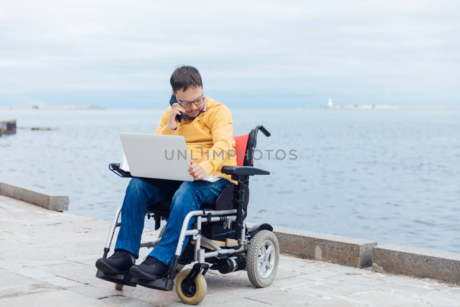 A man in a wheelchair came to the sea to work online on a laptop for business