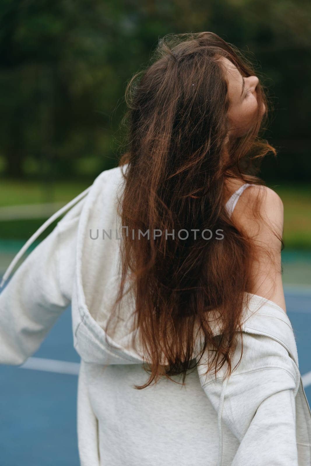 Carefree young woman with long hair, dressed in a grey hoodie, smiling and enjoying the outdoors during summer Captures a joyful, relaxed emotion with vibrant green background