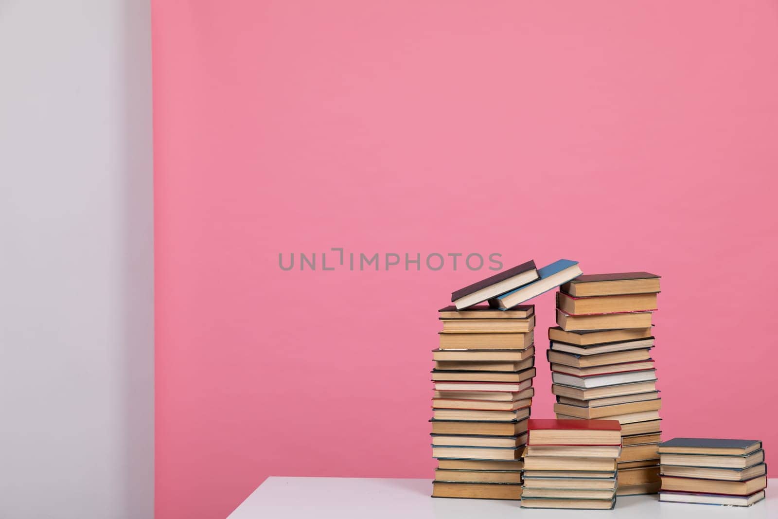 Stacks of old educational books for teaching in the library on a pink background at school