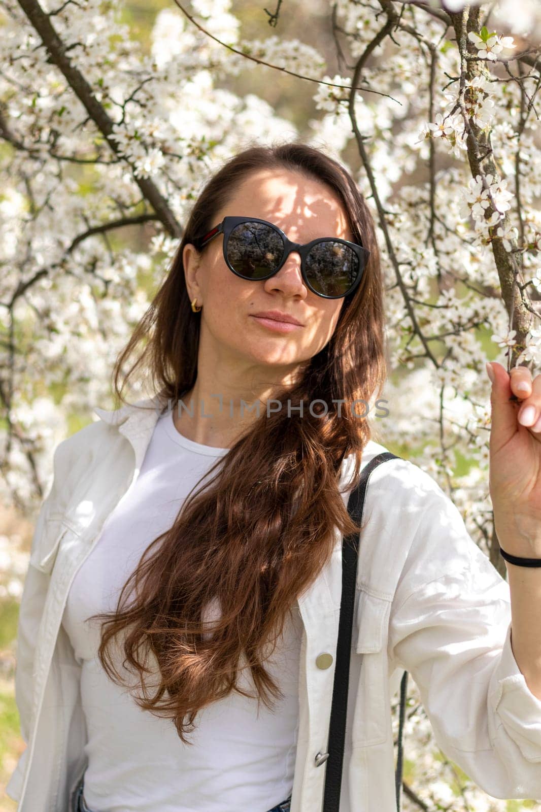 Beautiful woman poses for photo in the blooming with flowers garden