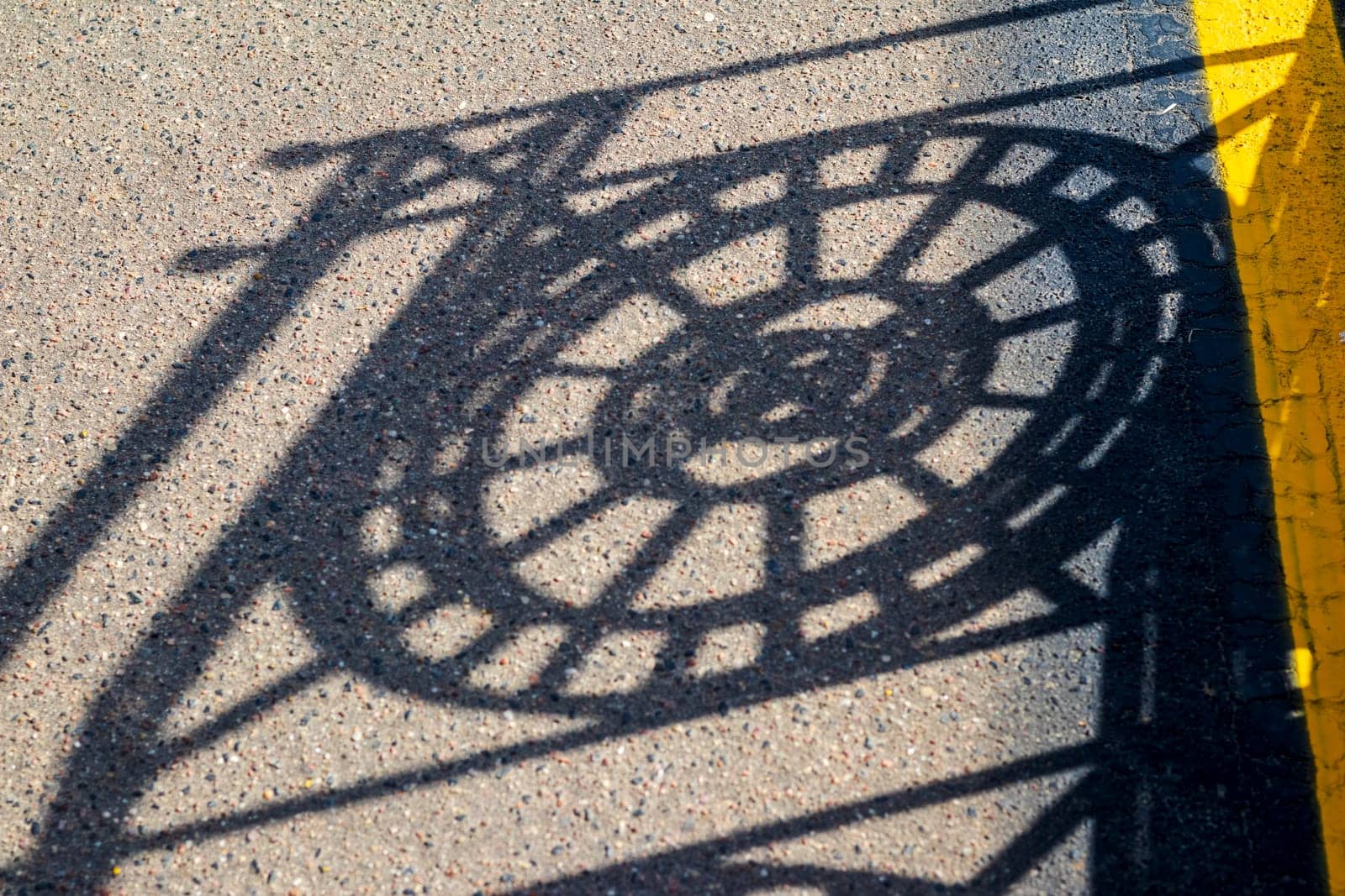 Shadow casting from the metal decorative fence to the asphalt