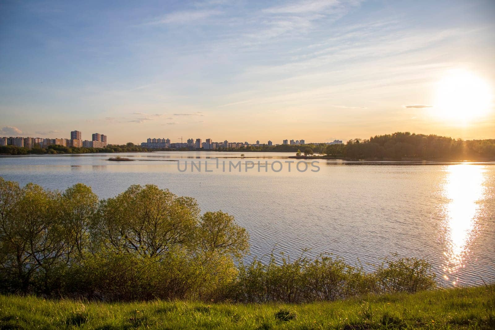 Sun is setting by the lake with city buildings on the background