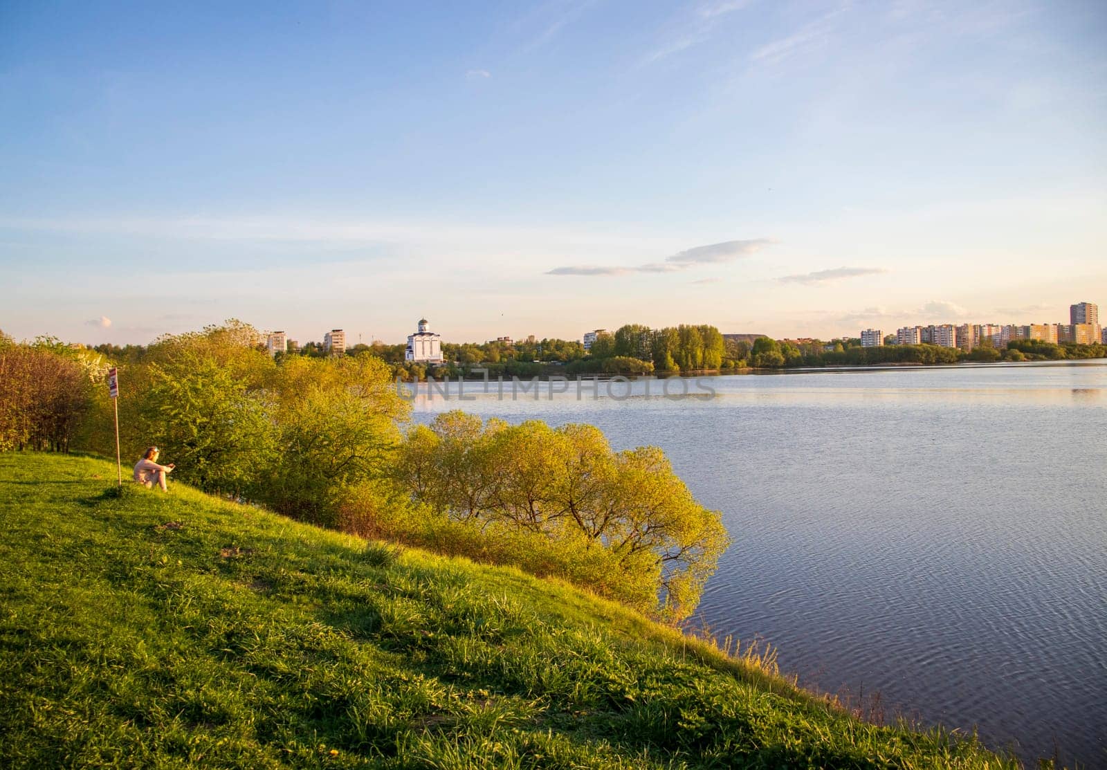 Minsk, Belarus - 05.04.2025 - Sun is setting by the lake with city buildings on the background