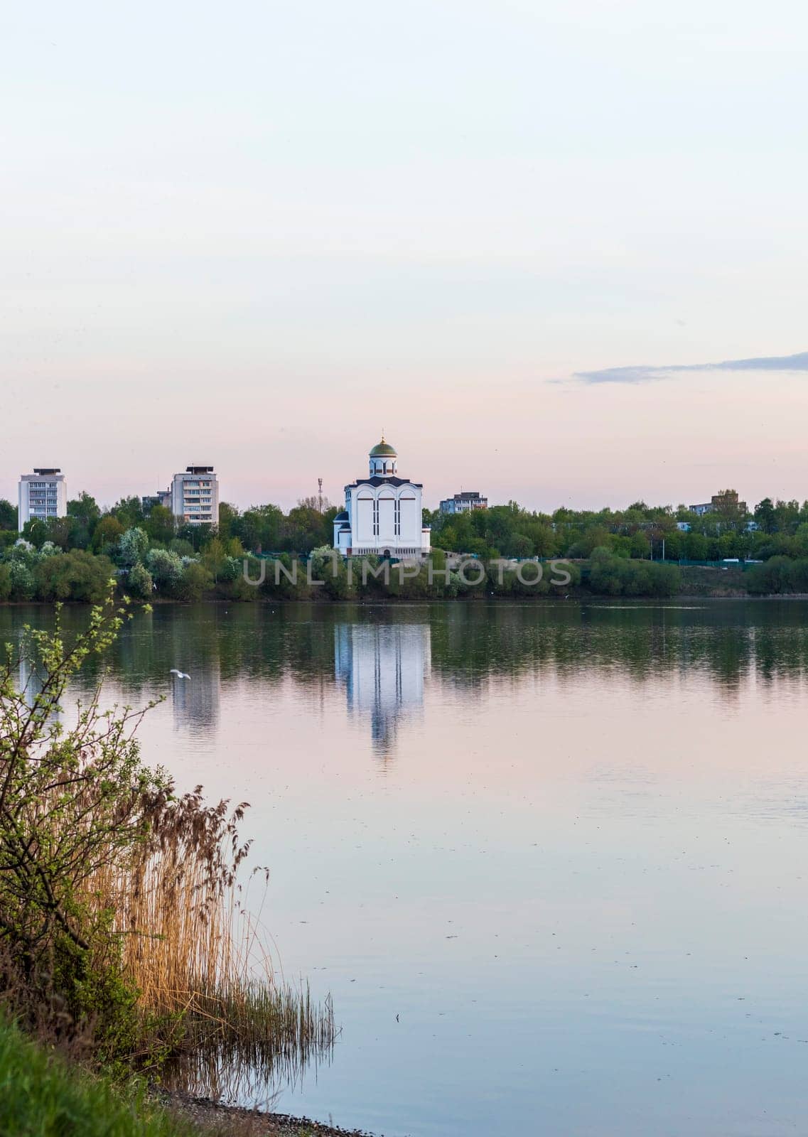 Sun is setting by the lake with city buildings and church on the background