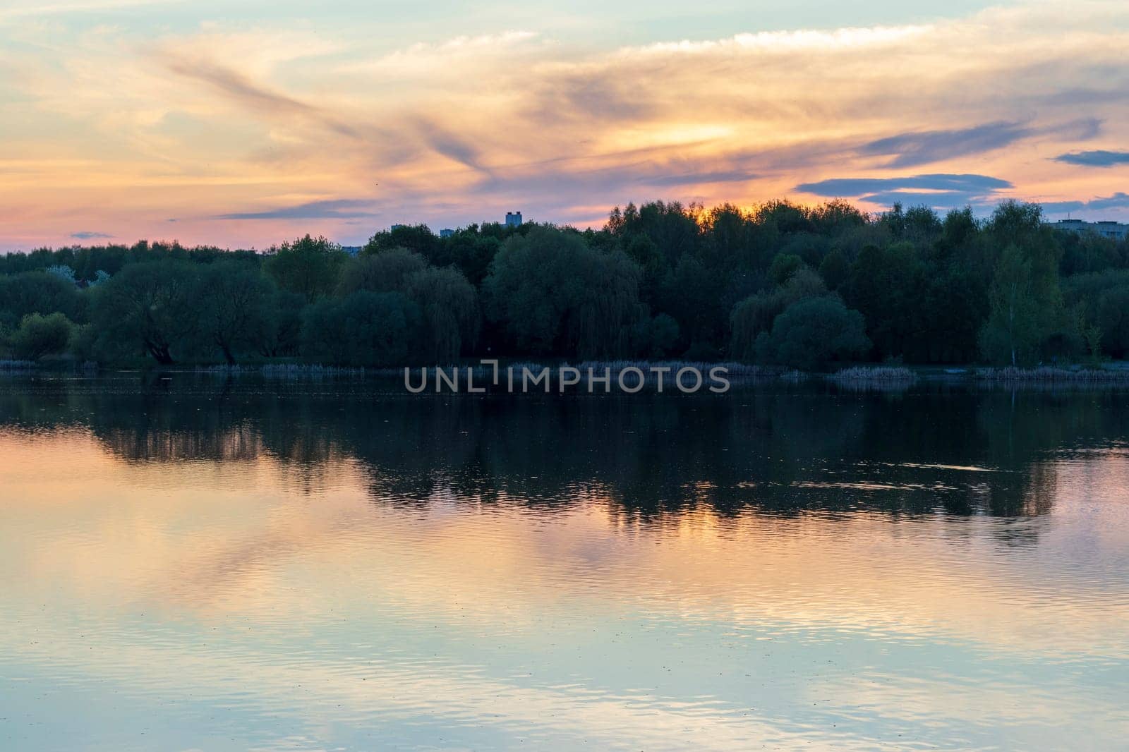 Sun is setting by the lake with city buildings on the background