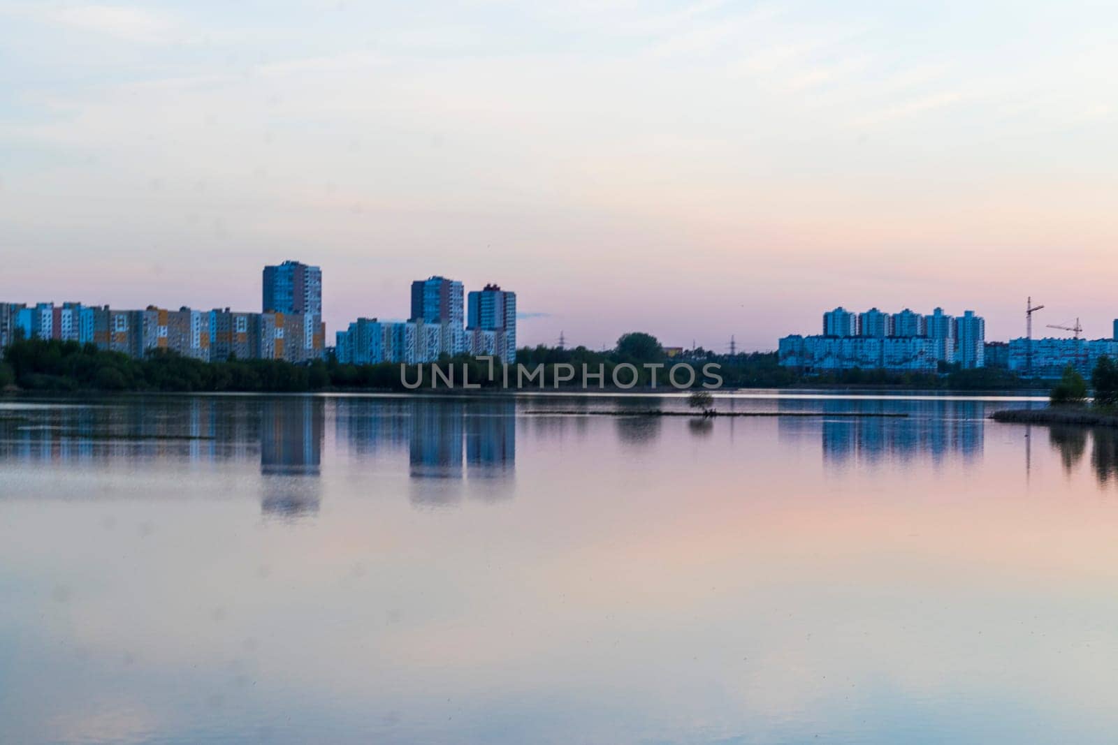 Sun is setting by the lake with city buildings on the background