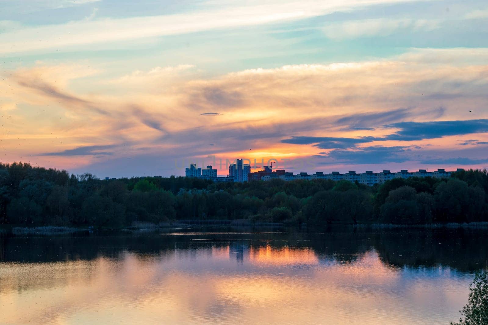 Sun is setting by the lake with city buildings on the background