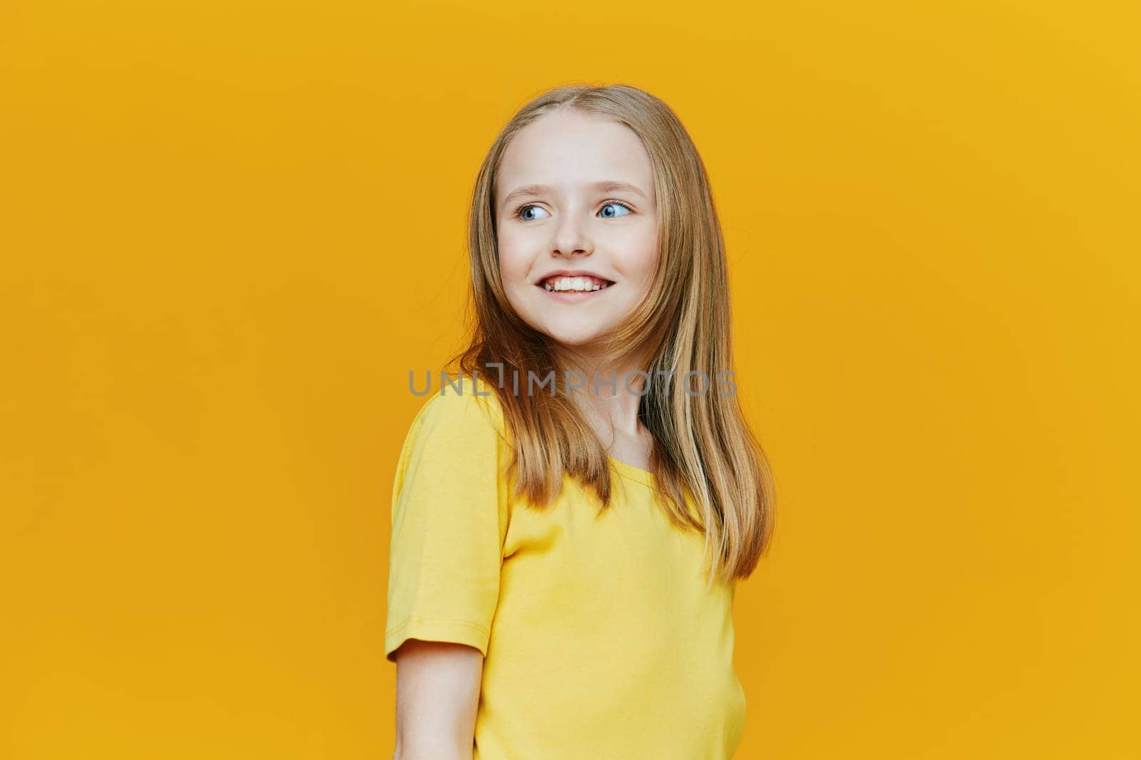 Joyful young girl with long hair smiling, dressed in yellow, set against a bright yellow background, embodying happiness and youthful energy in a fun, colorful atmosphere