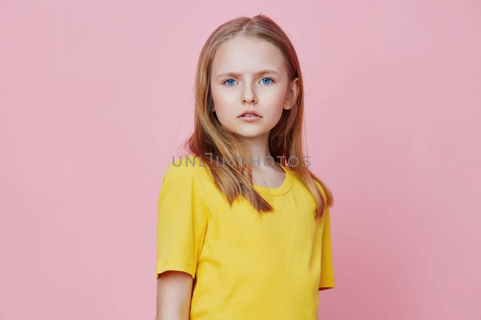 Portrait of a young girl with blonde hair in a yellow t shirt, standing against a pink background, showcasing innocence and youthfulness, ideal for themes of childhood and joy