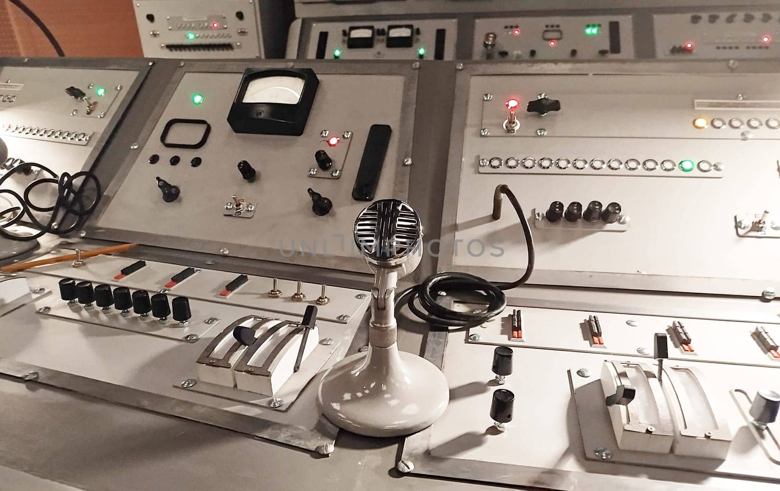 A vintage broadcasting studio showcases a control panel filled with various buttons, knobs, and levers. A classic microphone sits prominently at the center, symbolizing communication.
