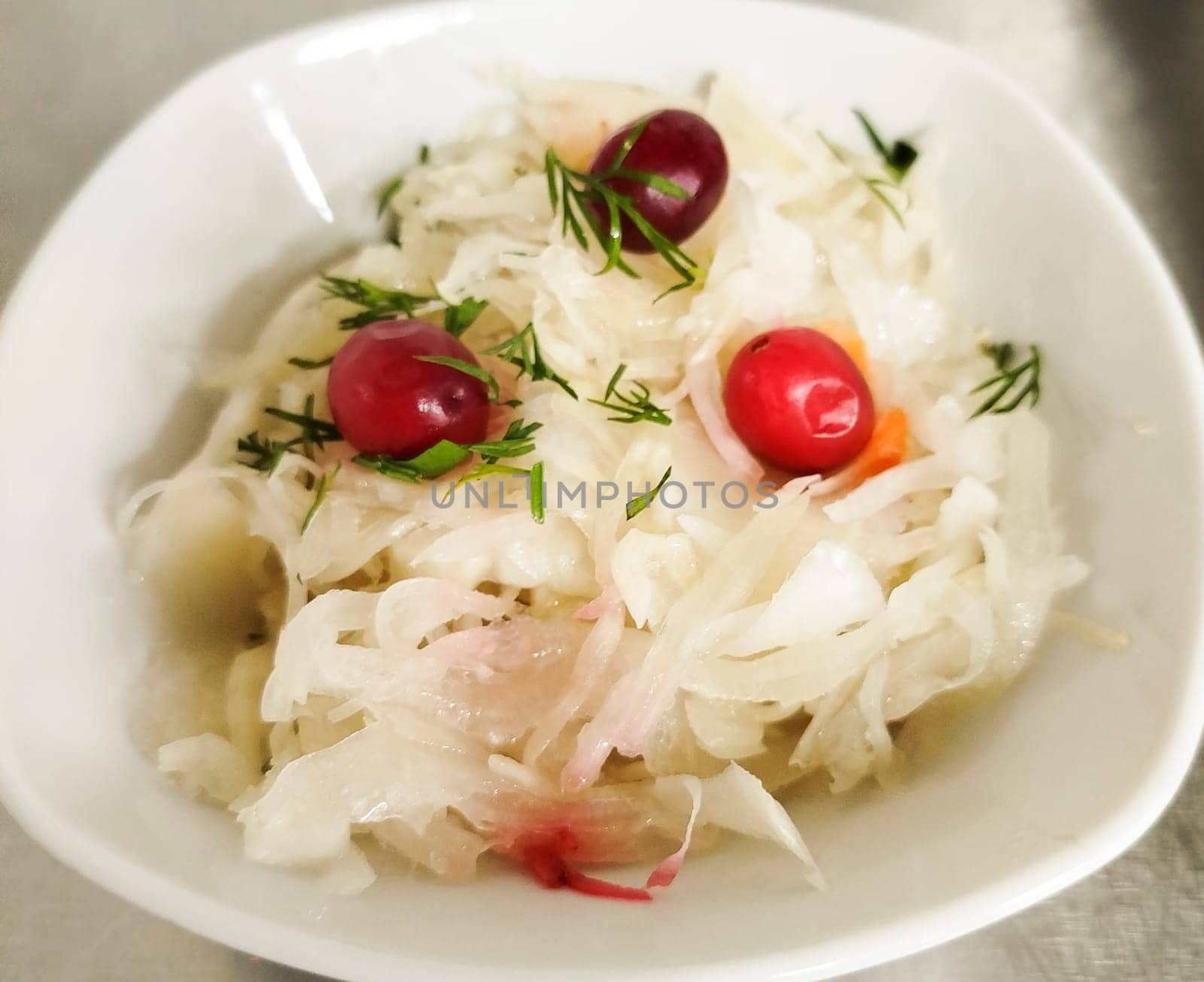 Crisp fermented cabbage salad is served in a white bowl, garnished with fresh herbs and vibrant berries. This dish showcases a unique blend of flavors and textures.