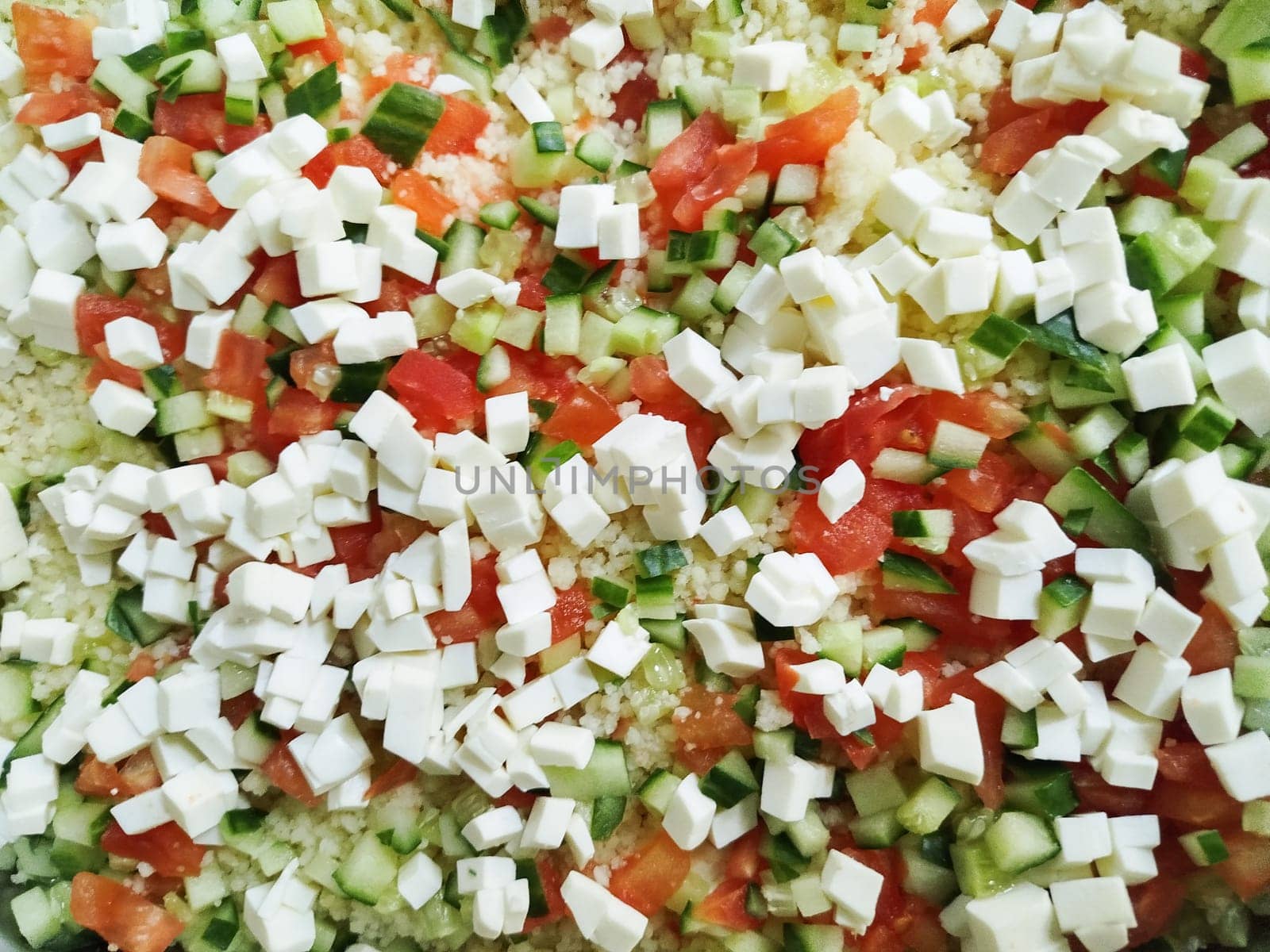 Colorful diced tomatoes and cucumbers are mixed with small cubes of cheese, creating a vibrant salad ready for tossing. This dish represents a healthy and refreshing meal option.