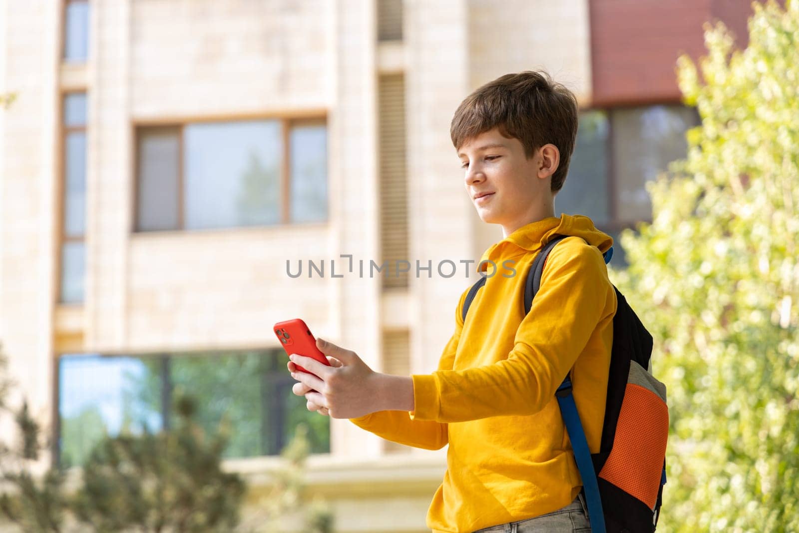 Teenage boy holds a smartphone and smiles in front of a high-rise building. Symbolizes the digital era, where technology shapes communication, learning, and modern life.