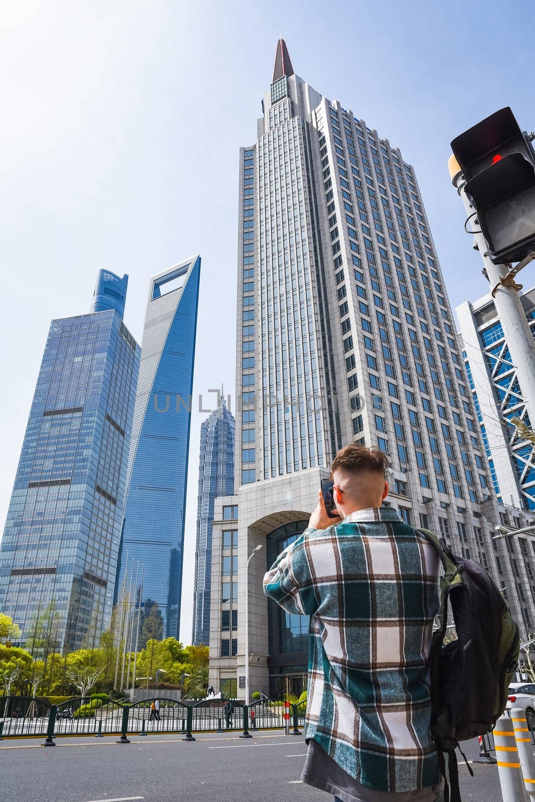 A male tourist in a casual shirt and backpack takes a smartphone photo of Shanghai’s futuristic skyline, showcasing travel blogging and social media moments in urban Asia.