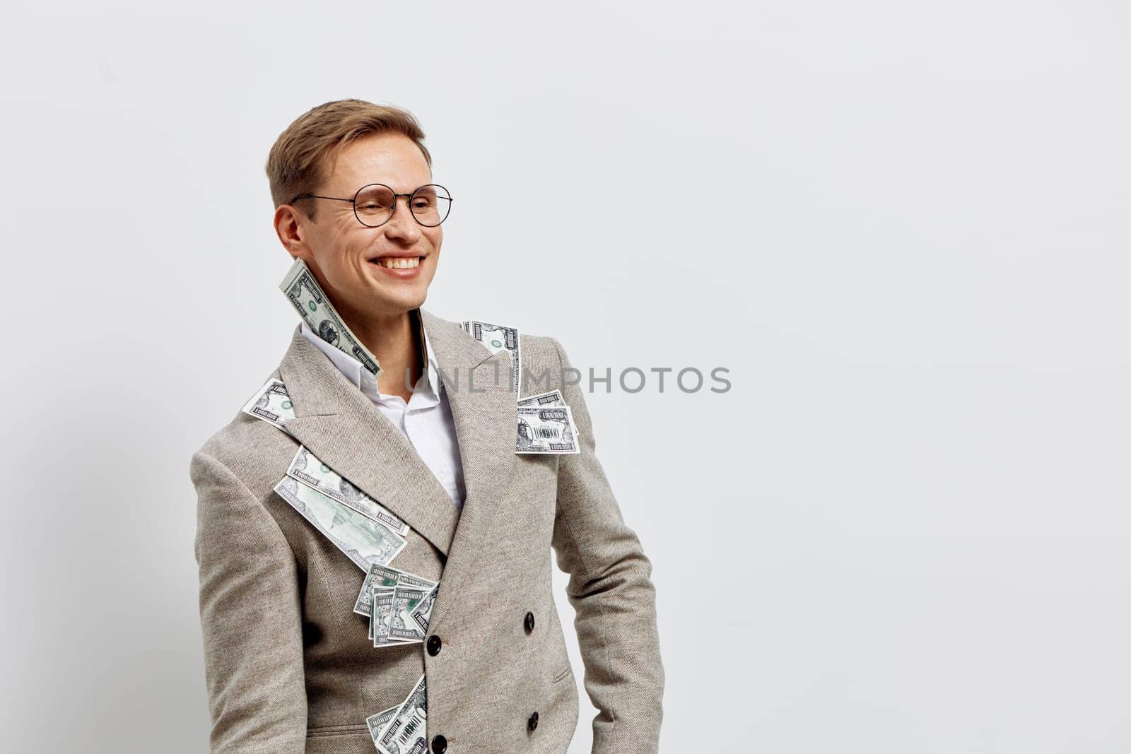 Smiling young caucasian man in stylish beige coat with money bills tucked in pockets and collar, looking confident and happy, symbolizing financial success, wealth, and digital nomad lifestyle concept on plain light background