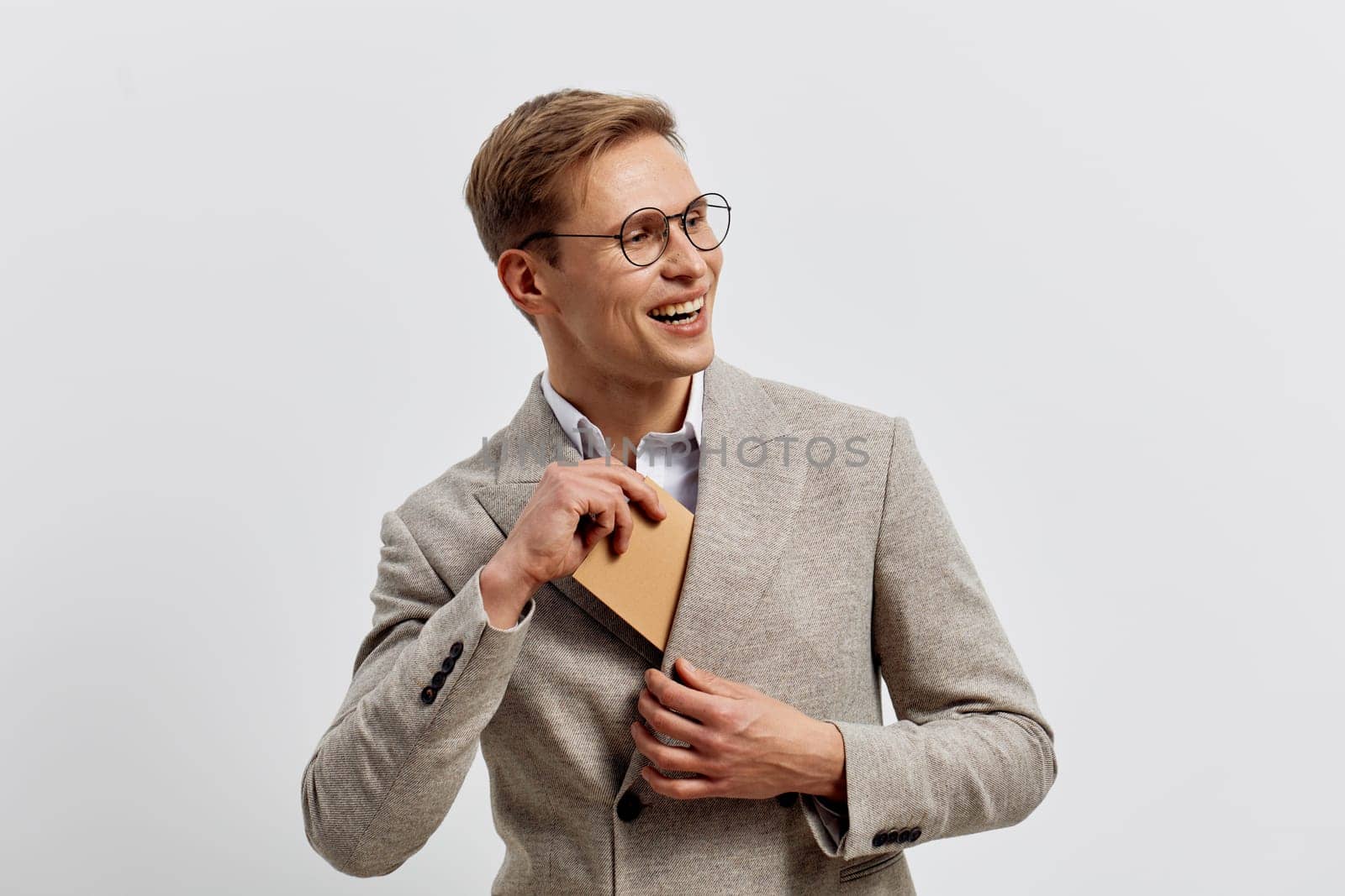 Happy smiling man with glasses dressed in a gray blazer holding a notebook, standing against a plain background. Genuine expression of confidence and positivity, ideal for business or education themes, modern professional look.
