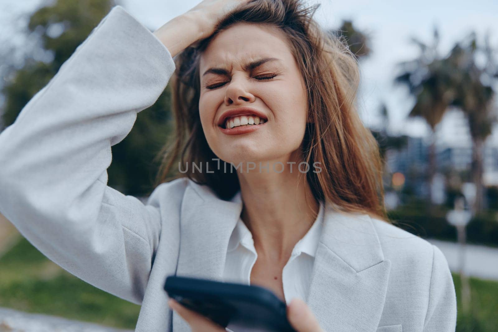 A businesswoman expressing frustration outdoors, wearing a stylish suit while holding a smartphone. The image captures the pressures of modern work life with a seasonally appropriate setting.