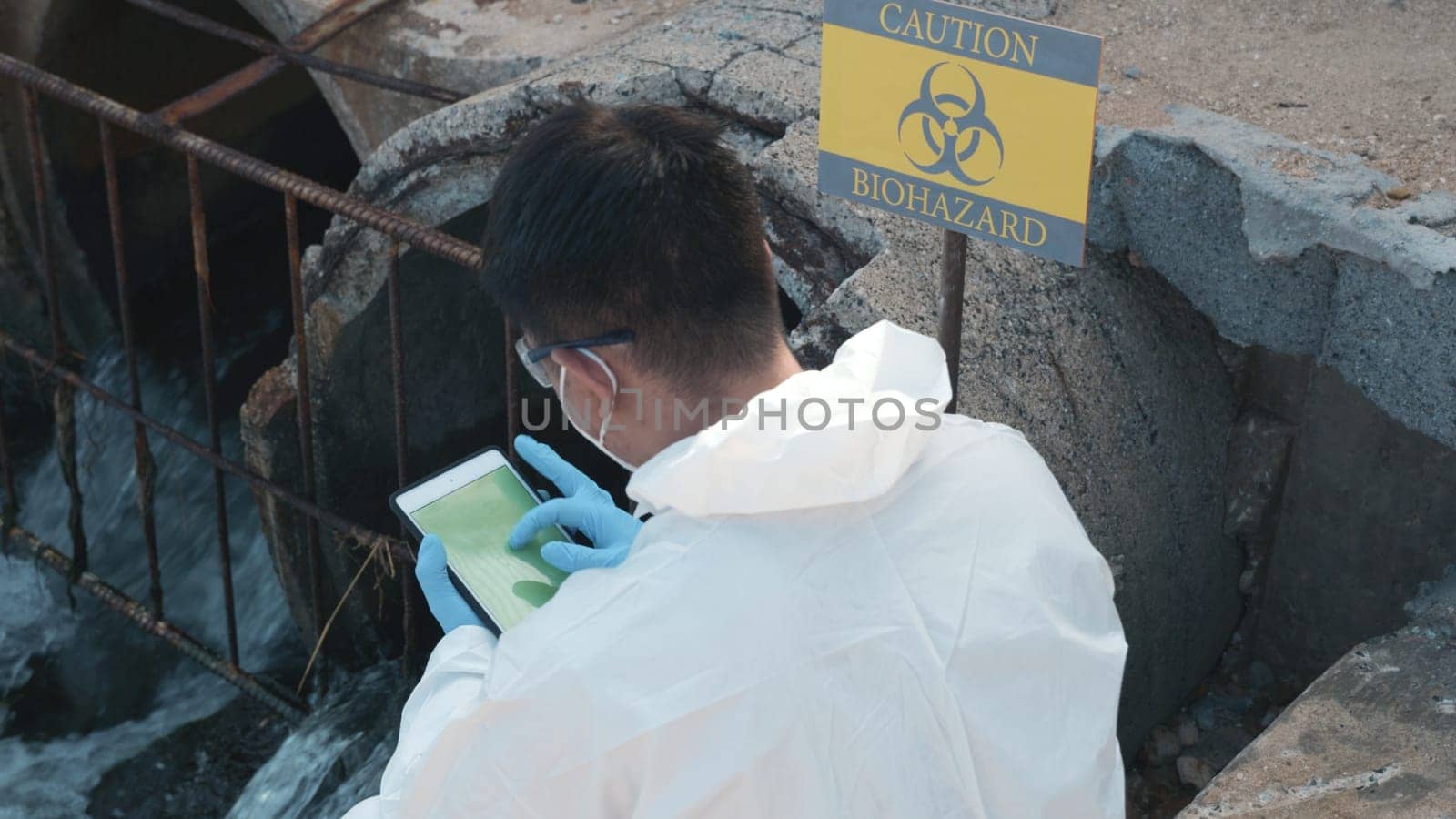 Ecologist sampling water of toxic chemicals from river touching screen on digital tablet, Biologist wear protective suit and mask collects sample of waste water from industrial, problem environment