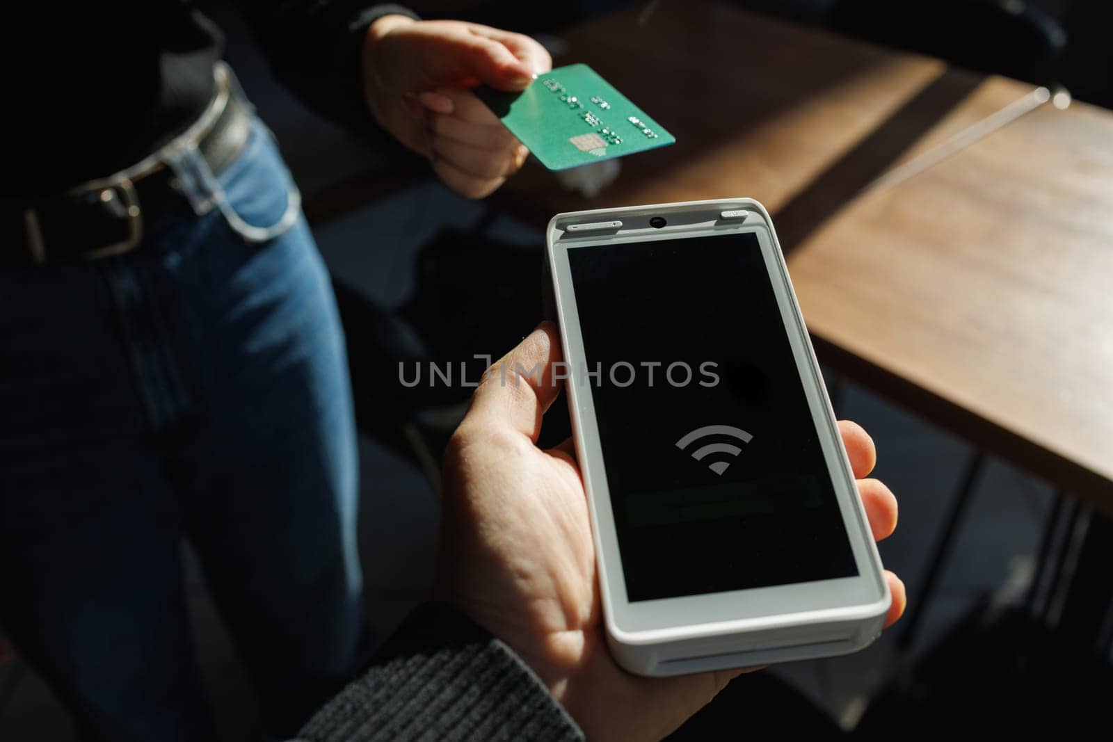 Close-up of wireless payment with green credit card and contactless POS terminal in a modern cafe setting.