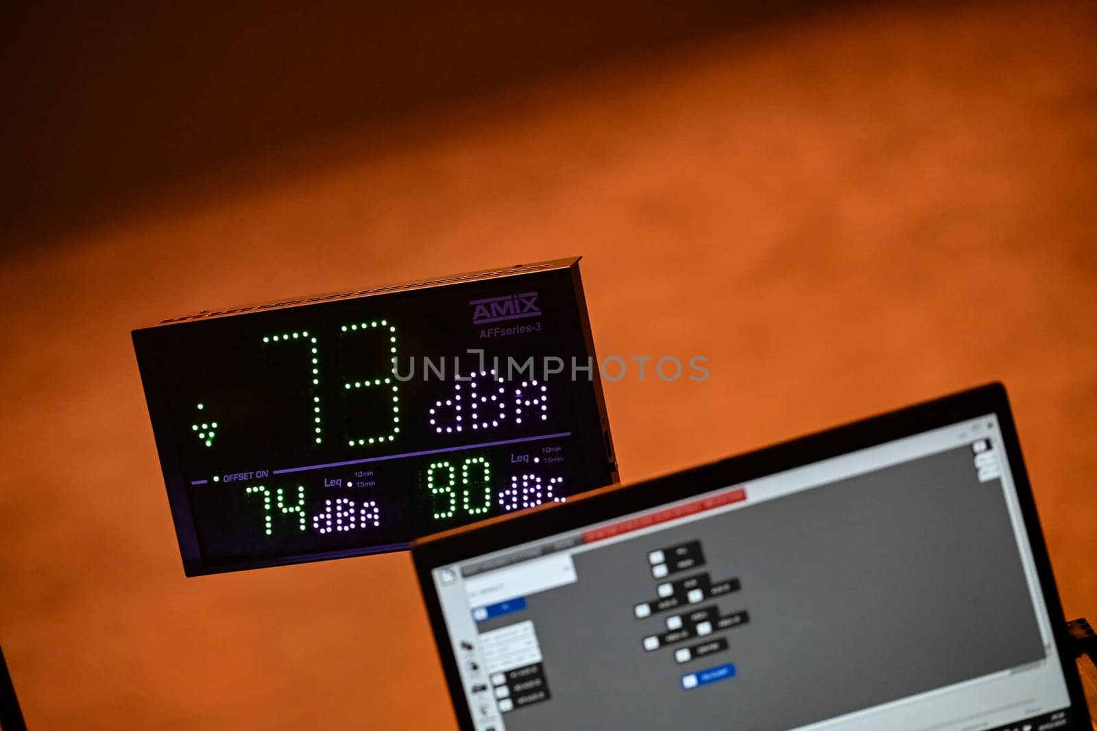 Sound level is monitored at a concert, showing 73 dBA on a digital display. A laptop runs software for tracking decibel levels as part of audio management.