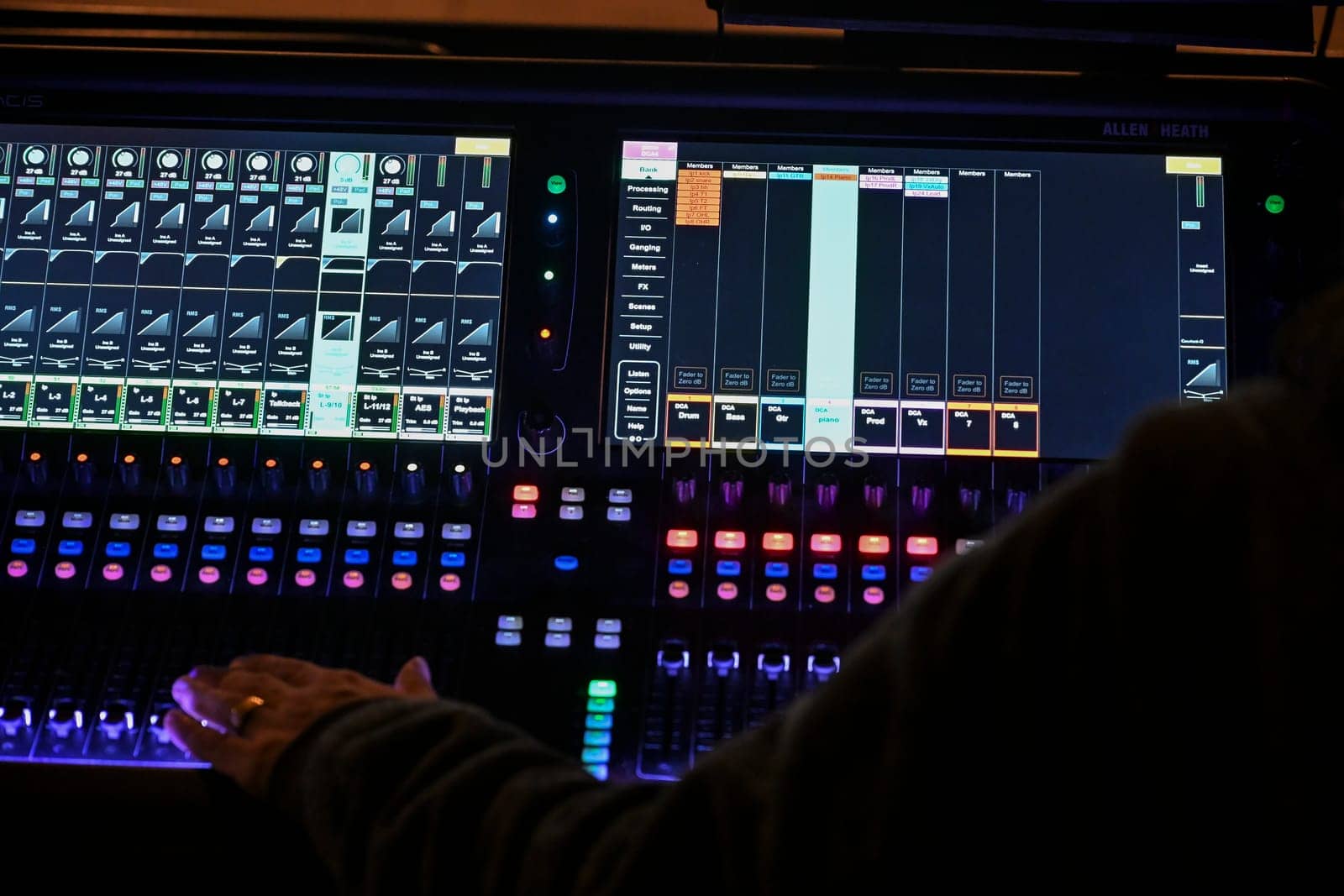 France, April 2025: Focused sound engineer adjusts sliders and knobs on a digital mixing console while preparing for a performance in a lively venue atmosphere.