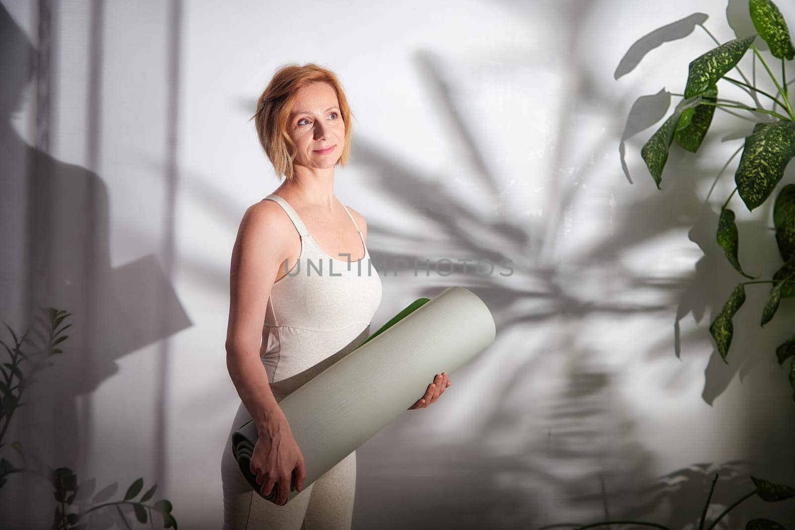 Practitioner holds a yoga mat with a relaxed expression, poised to begin a calming yoga session in a tranquil indoor environment.