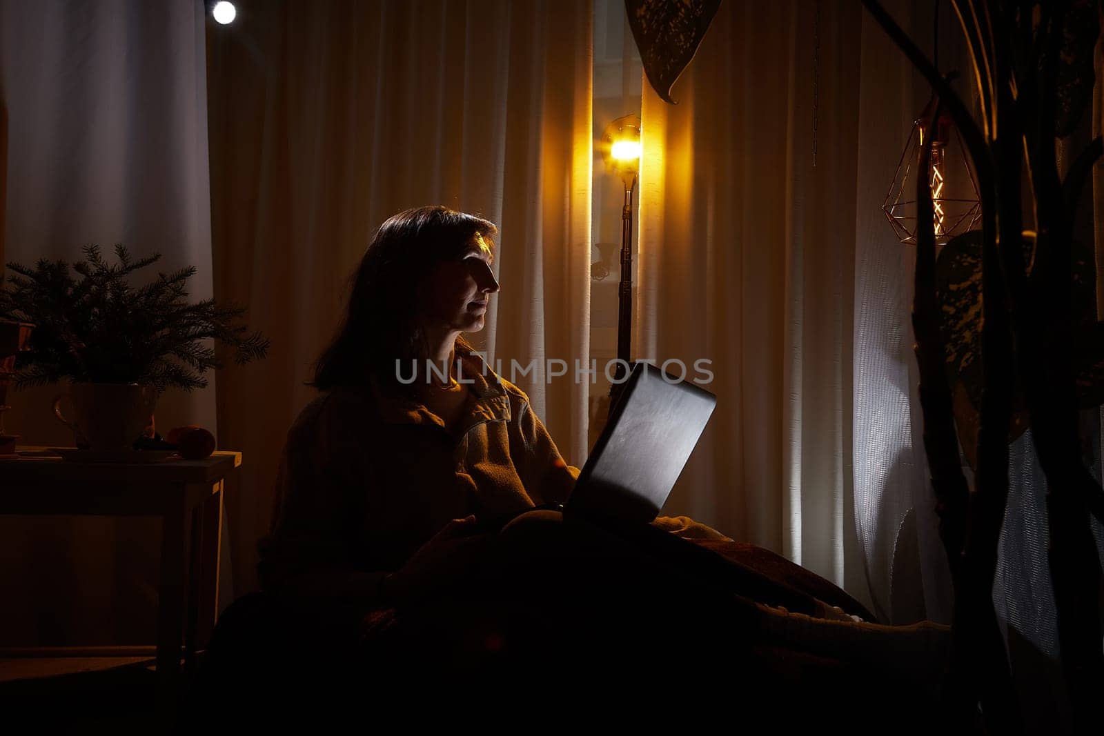 In a warm and inviting apartment, a middle-aged woman relaxes in the evening, focused on her laptop, embracing a moment of solitude.