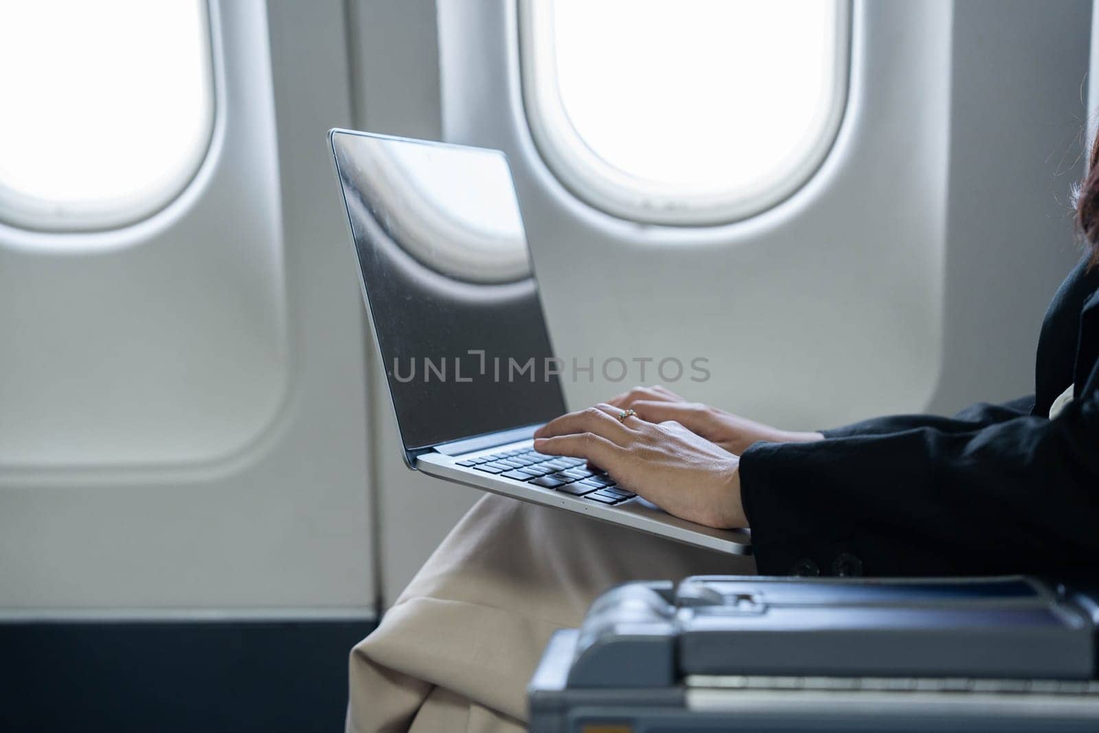 A businesswoman focused on her laptop while flying, showcasing modern work habits and the ability to work while traveling.