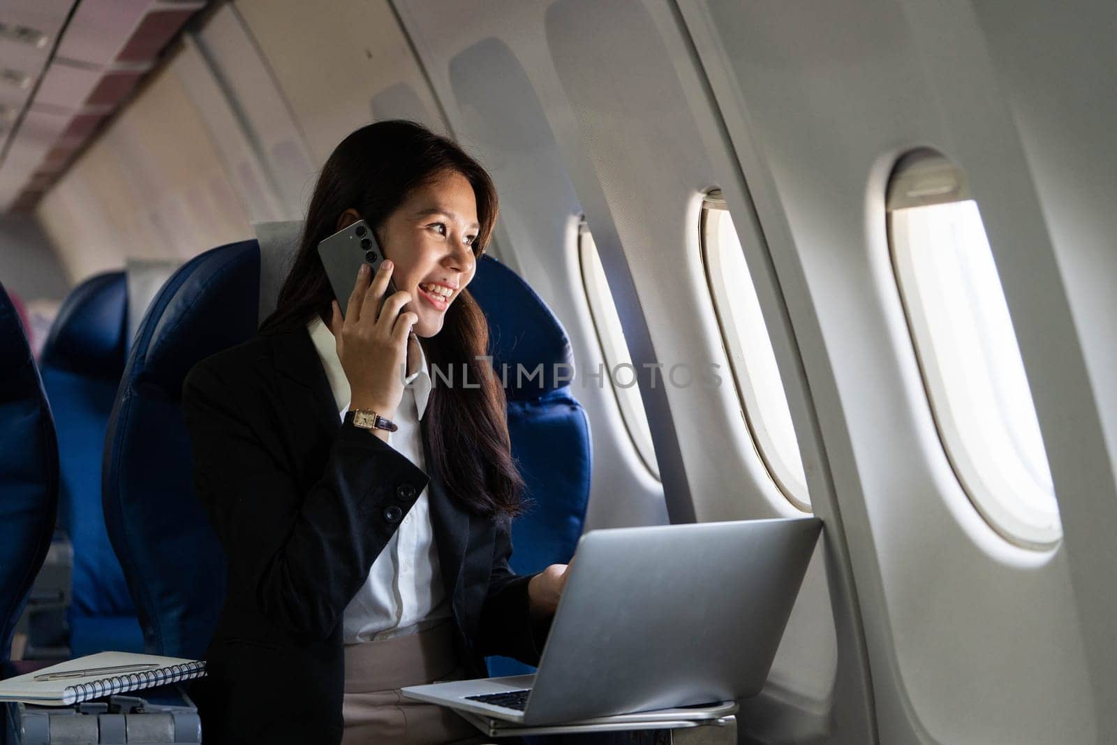 A young professional woman smiles while on a phone call during her flight, capturing the positivity of business travel.